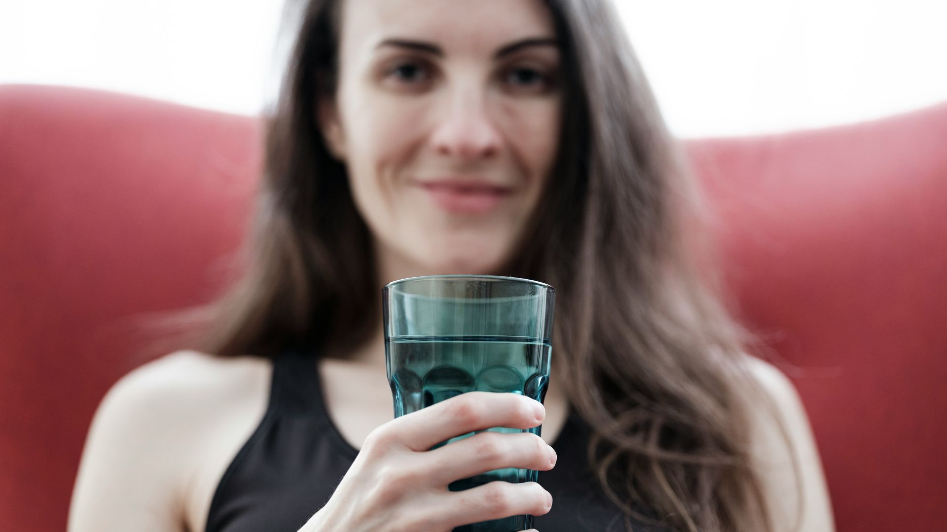 A woman is about to drink a transparent glass of water.