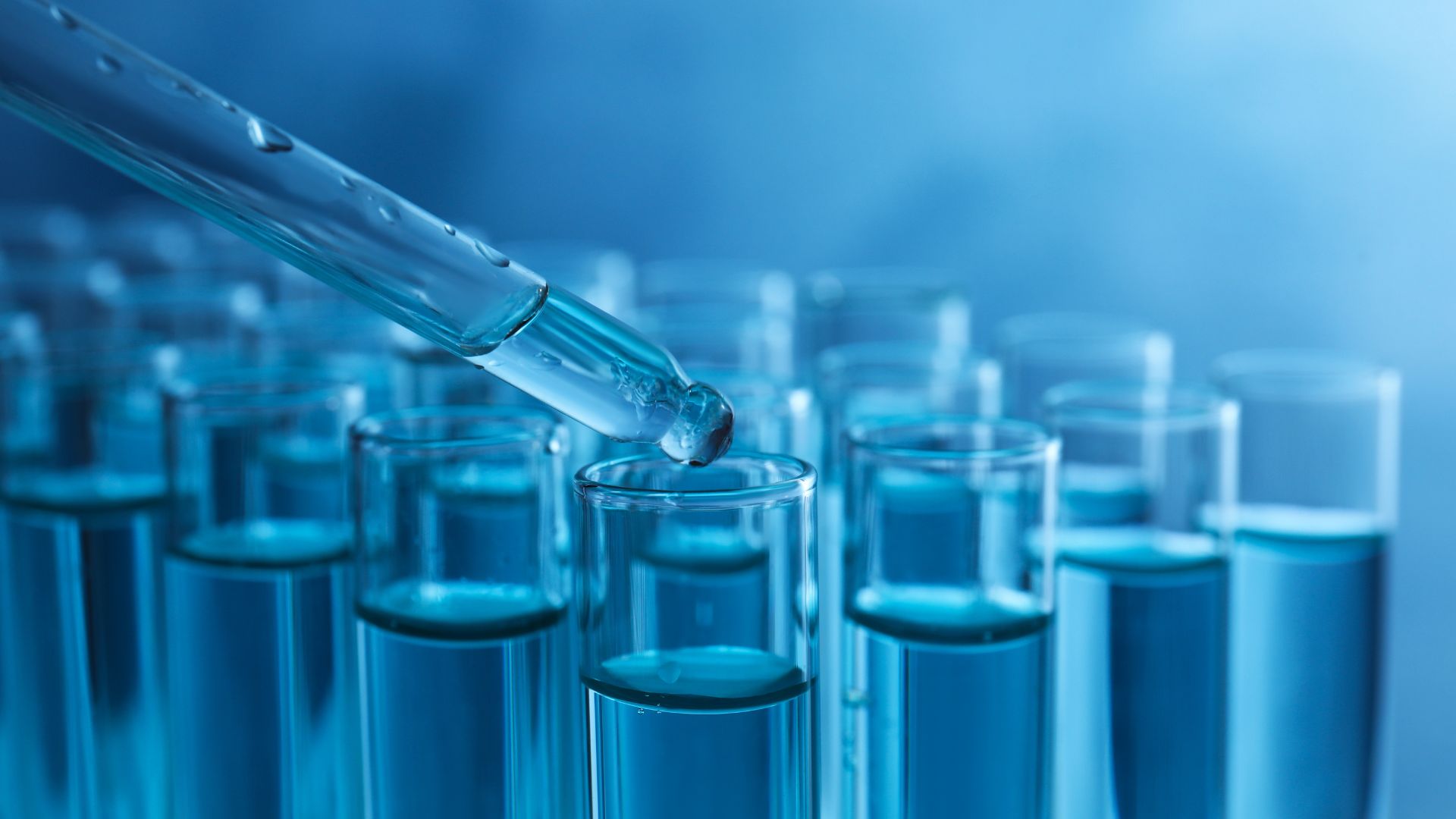 Dropping sample into test tube with liquid on blue background, closeup.