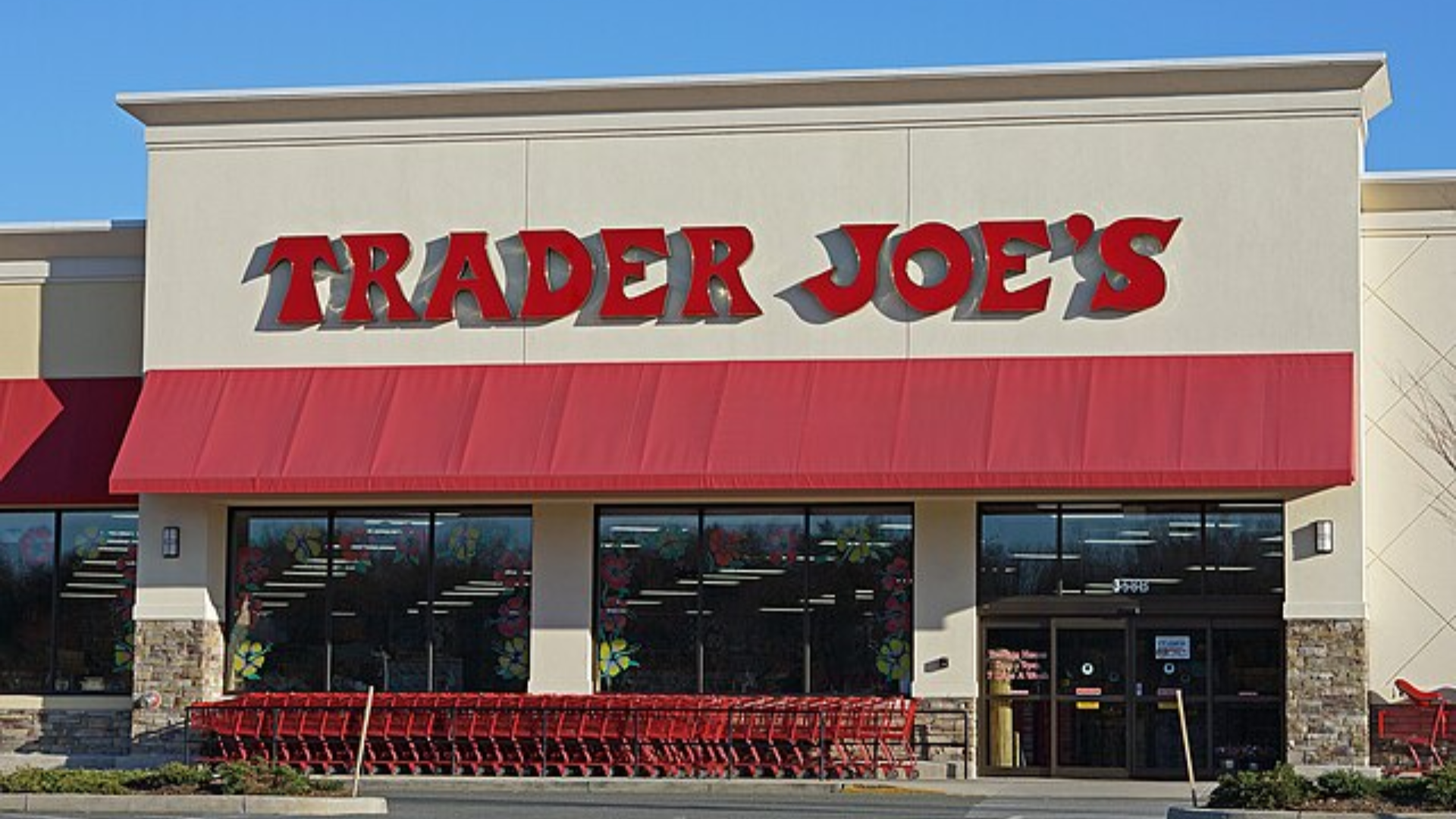 The exterior storefront of a Trader Joe's grocery store featuring its iconic red logo and red awnings.
