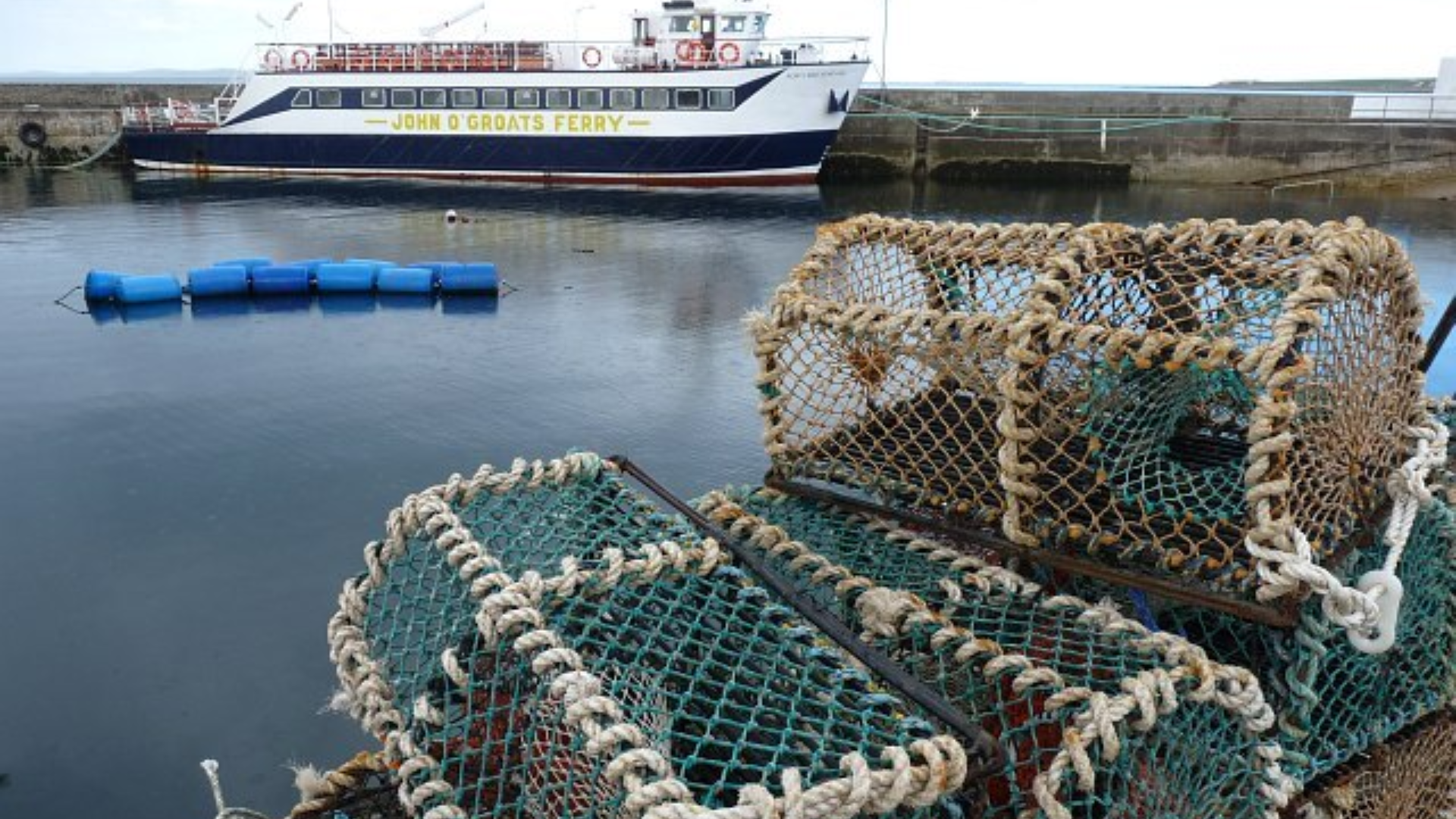 Drayton Harbor with Lobster traps stacked on a pier in the foreground with a Ferry docked in a harbor behind them.
