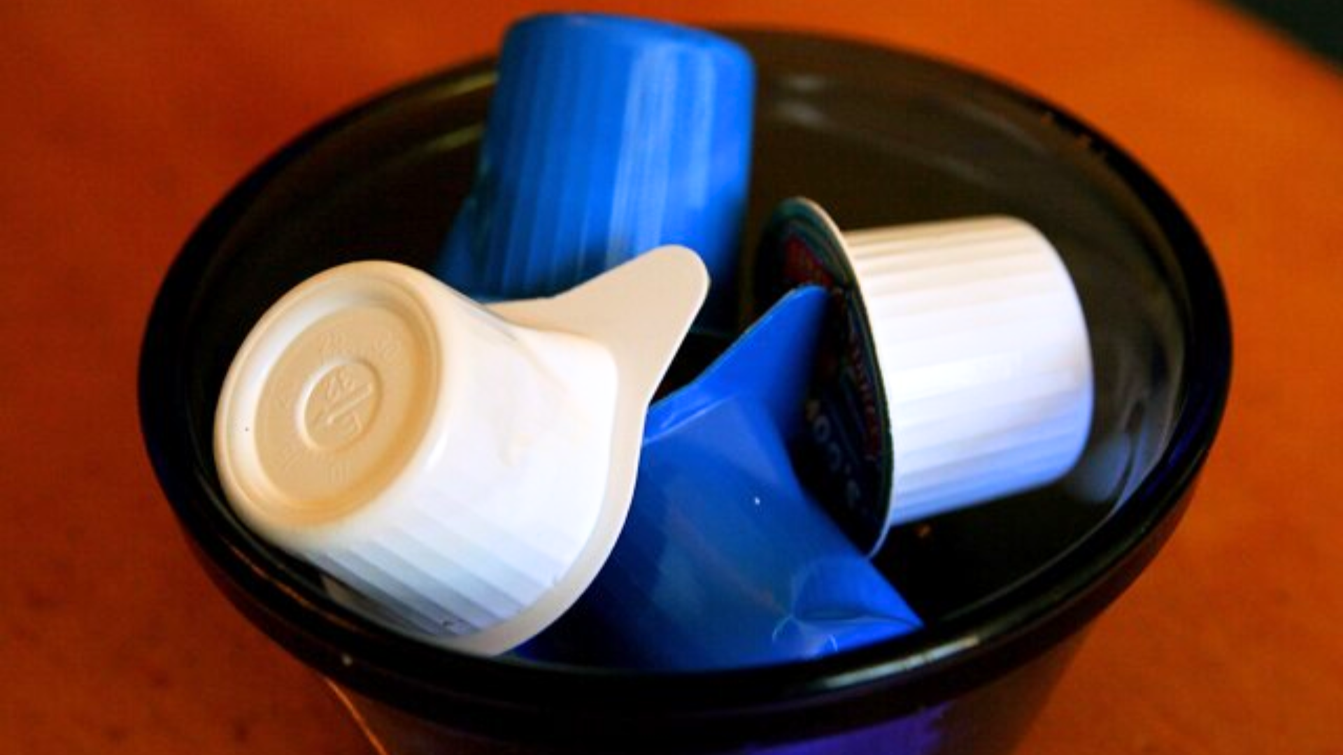 A black bowl filled with several blue and white individual coffee creamer pods.