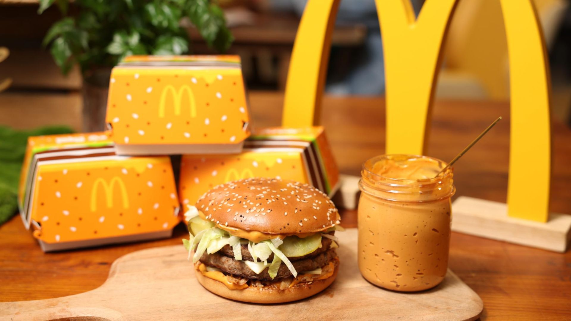Mcdonald's Big Arch next to the sauce, presented on a wooden board with its packaging at the back.