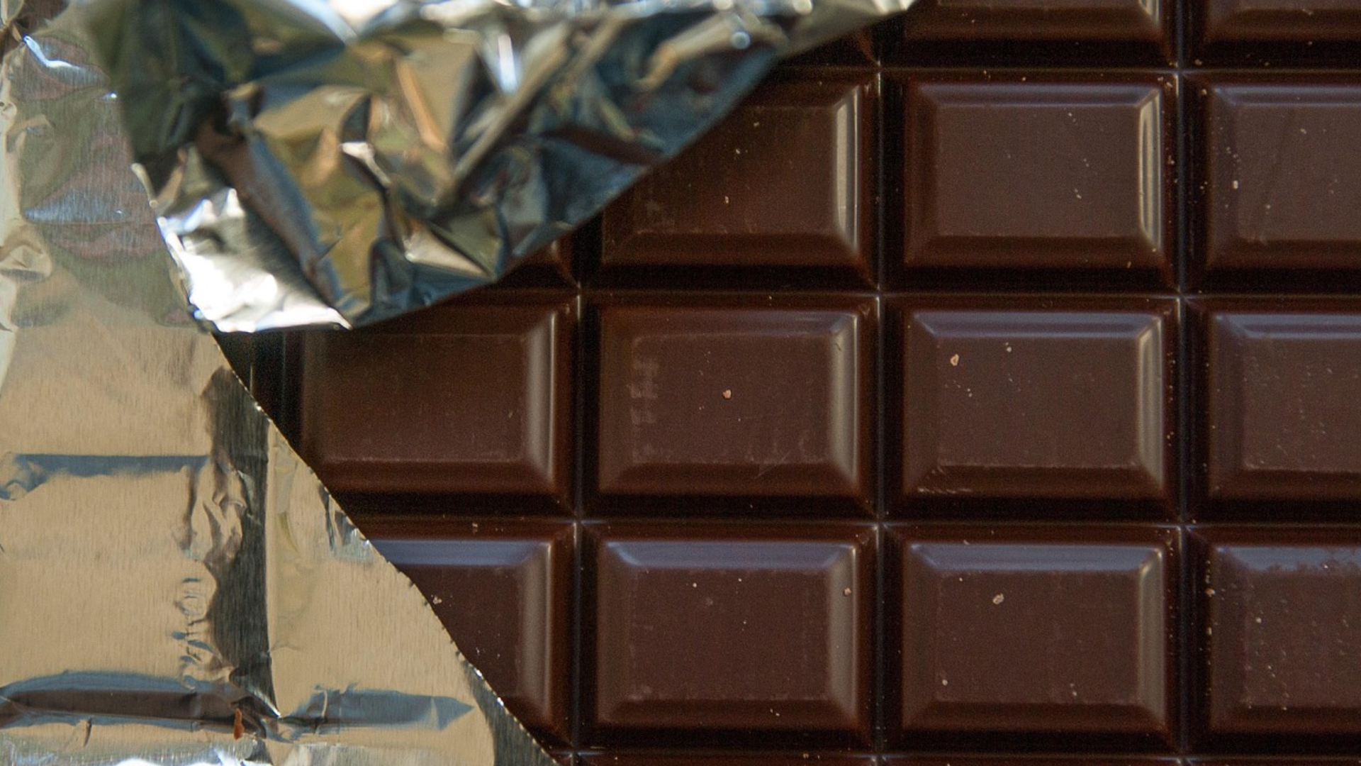 A dark chocolate bar partially unwrapped from silver foil.