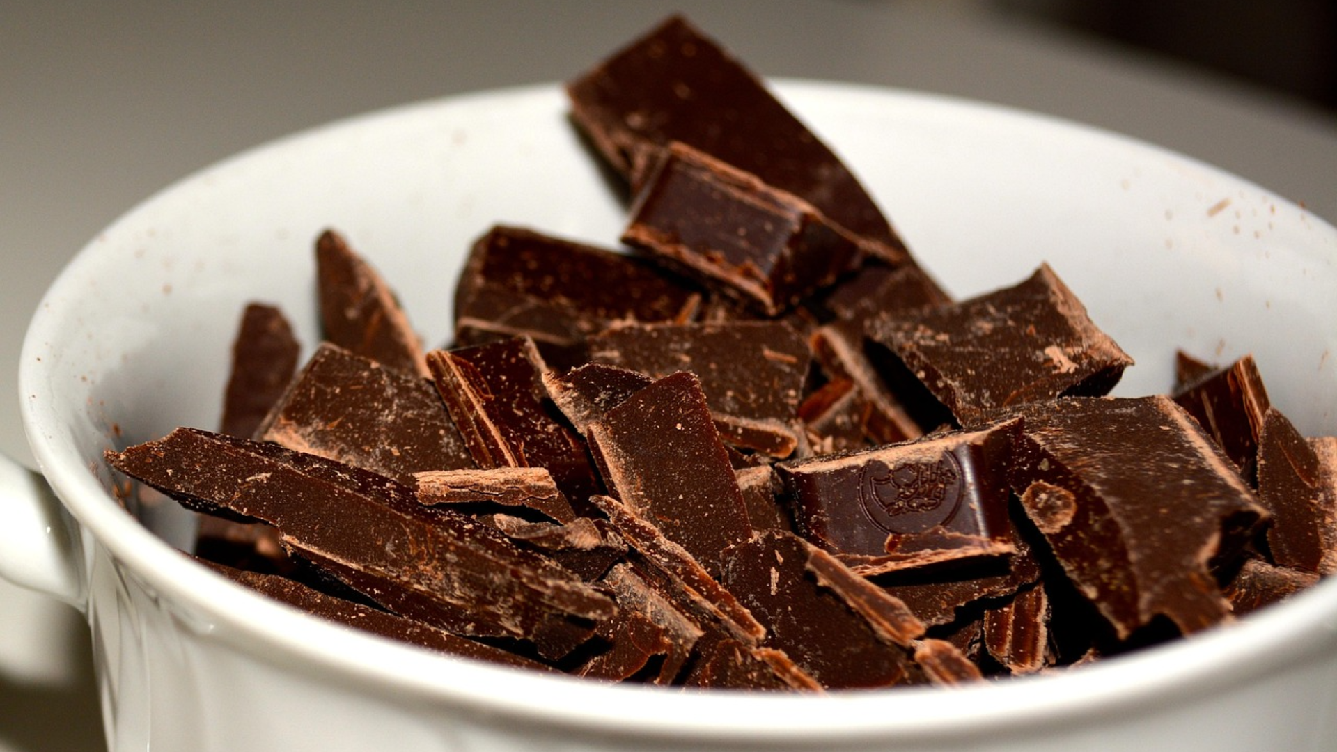 A white ceramic bowl filled with broken shards and chunks of dark chocolate.