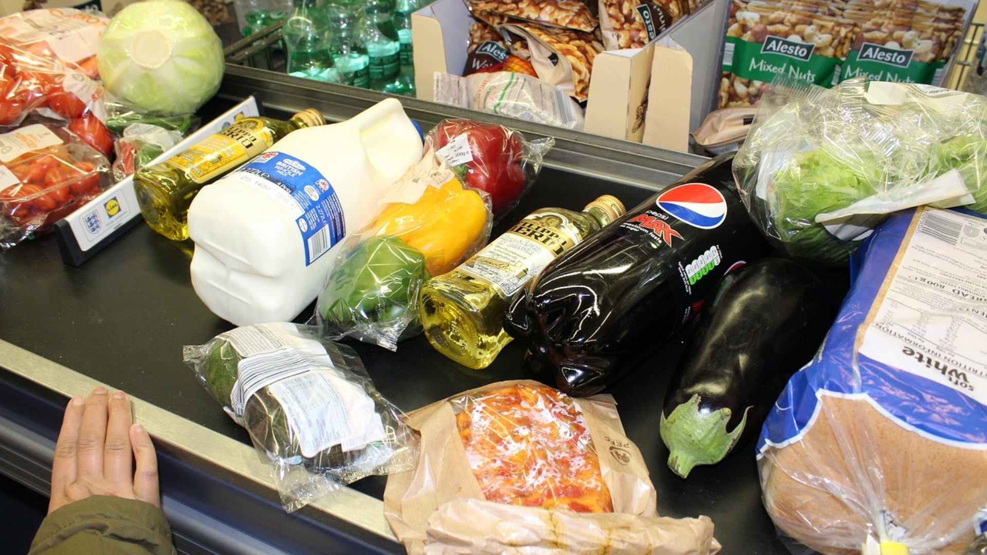 Various groceries, including milk, peppers, bread, and soda, on a supermarket checkout conveyor belt.