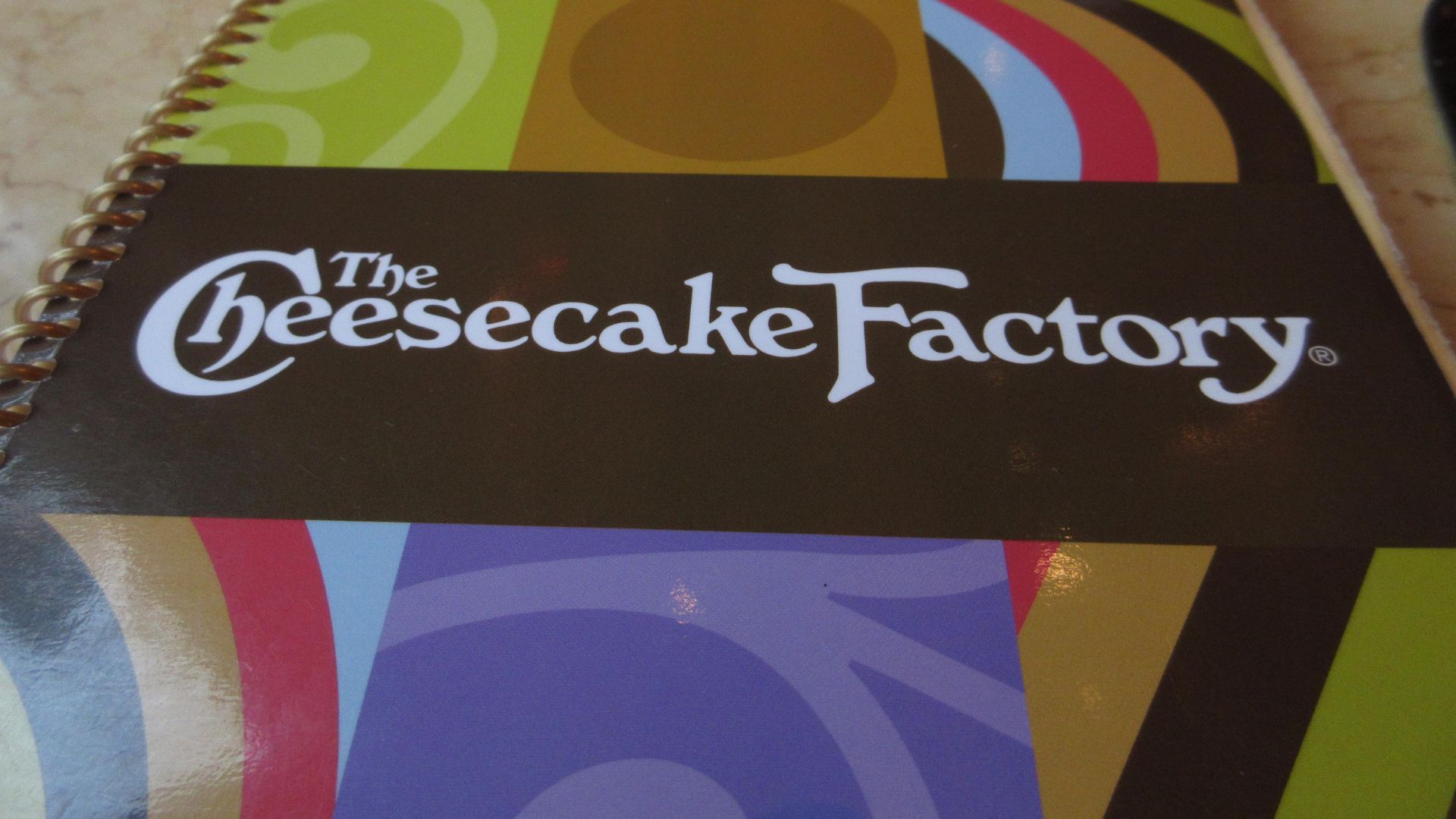 Menu cover for The Cheesecake Factory's menu, featuring a colorful geometric pattern and the restaurant's logo.