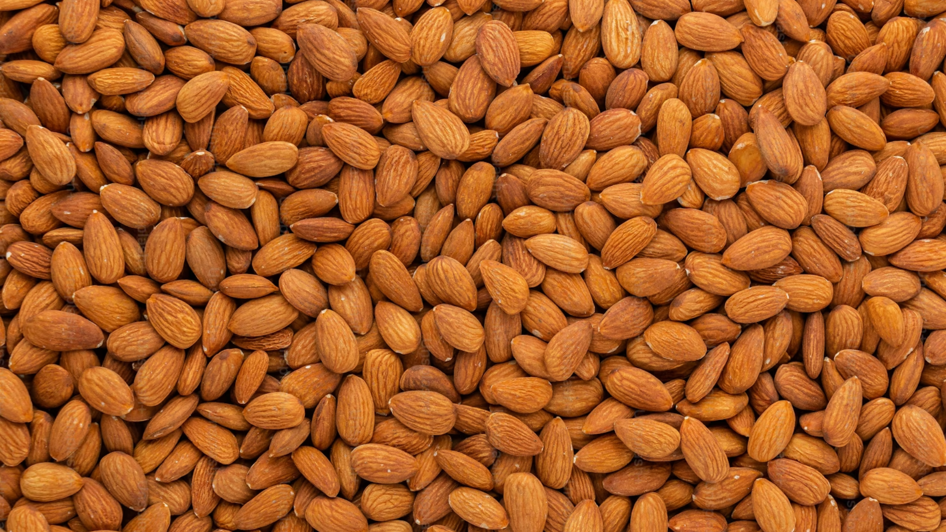 A close-up, full-frame view of raw whole almonds piled together, showing their textured brown skins.