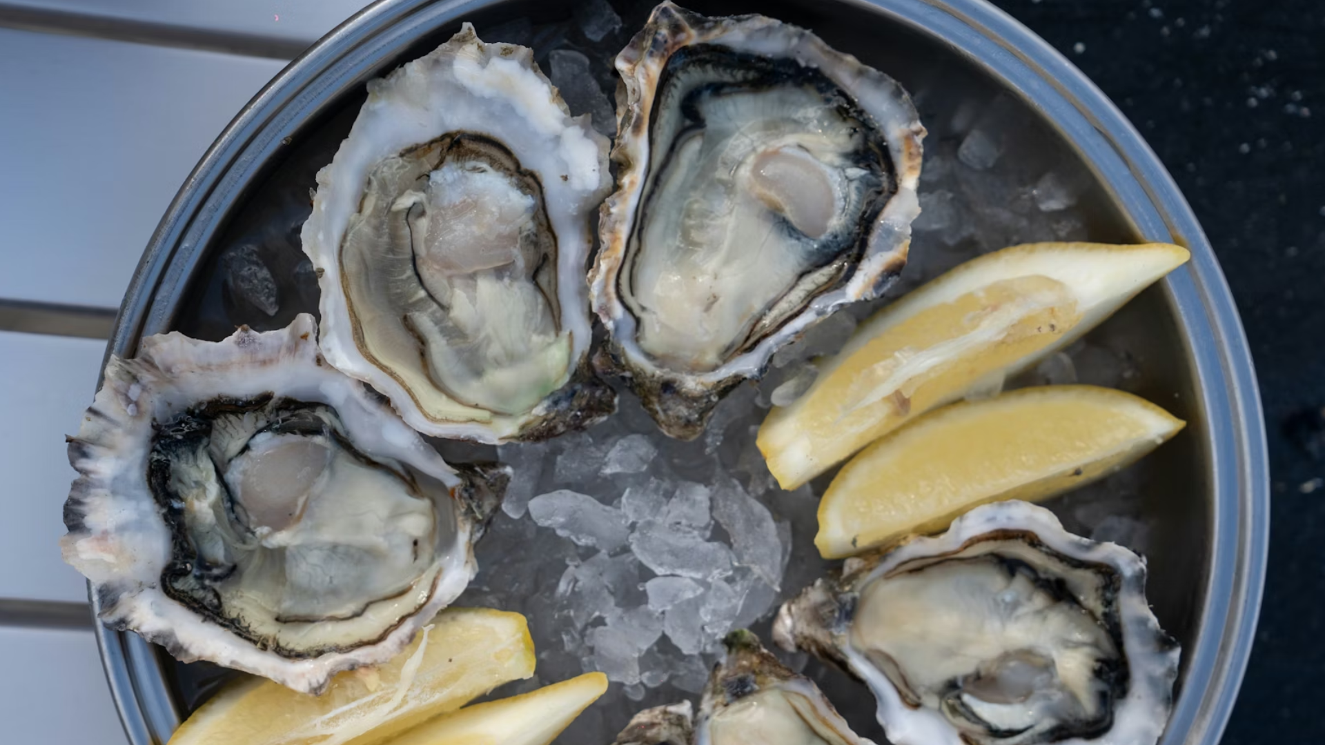 Overhead view of fresh raw oysters on the half shell served on ice with lemon wedges in a metal platter.