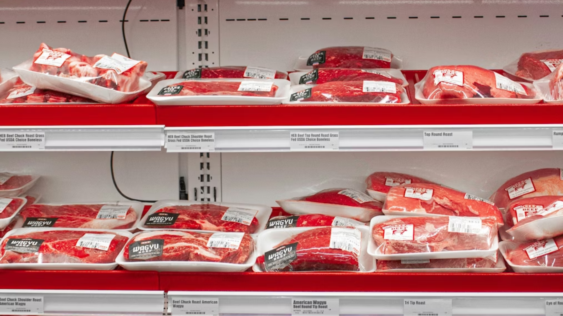 Packages of raw beef displayed on red shelves in a grocery store meat department.