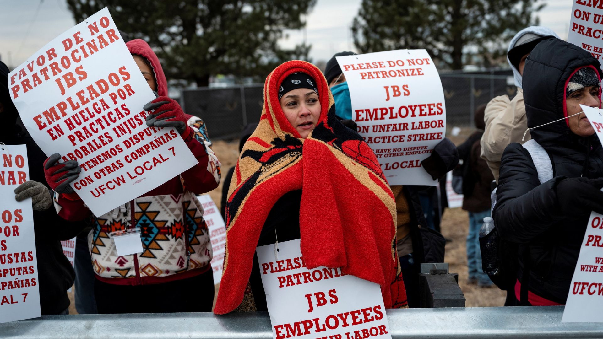 Protestors in winter clothing and blankets hold signs in English and Spanish, advocating against unfair labor practices at JBS.