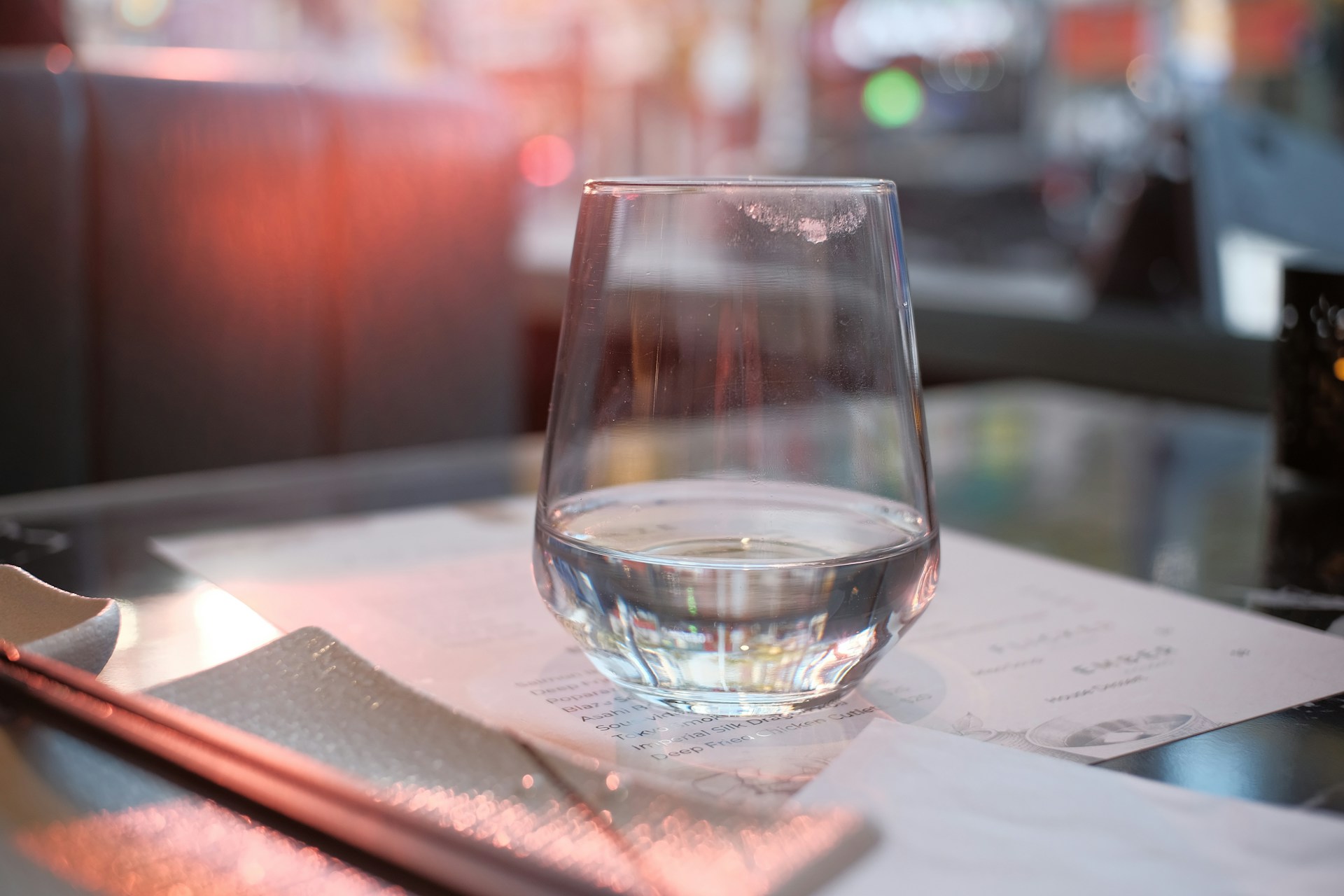 Glass of water on a table with a menu and napkin in a restaurant setting.