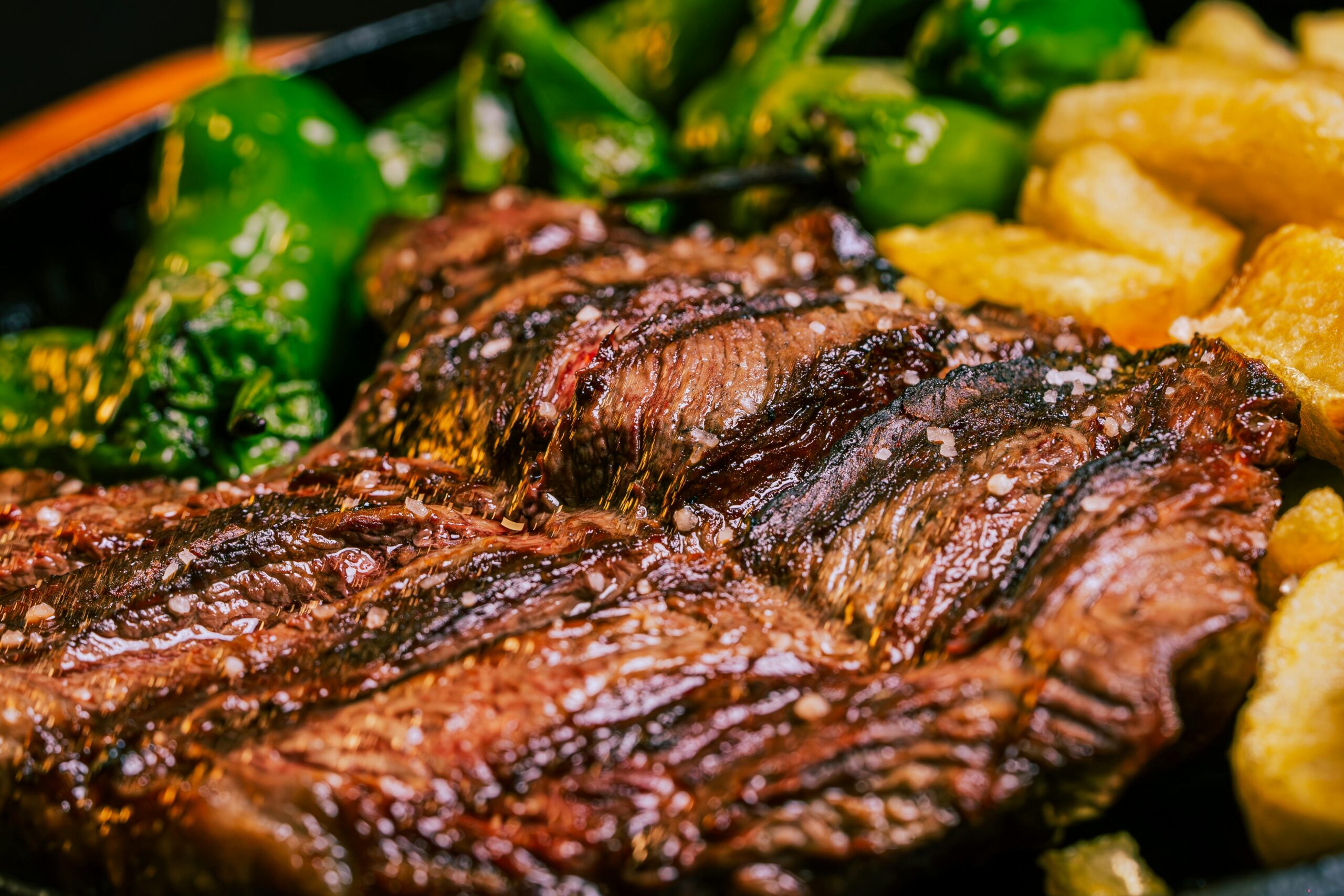 Grilled steak with peppers and potatoes on plate.