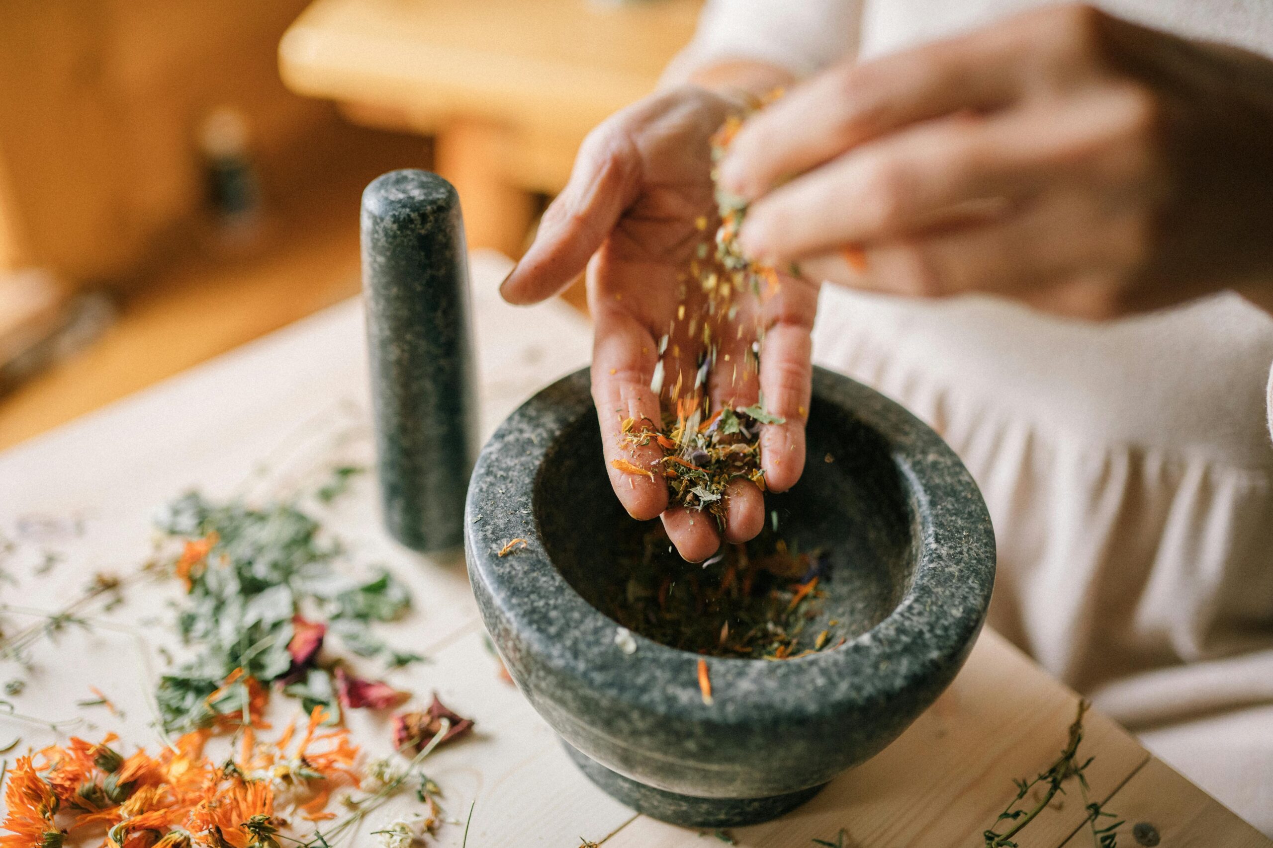 Hands sprinkling dried herbs into a stone mortar.