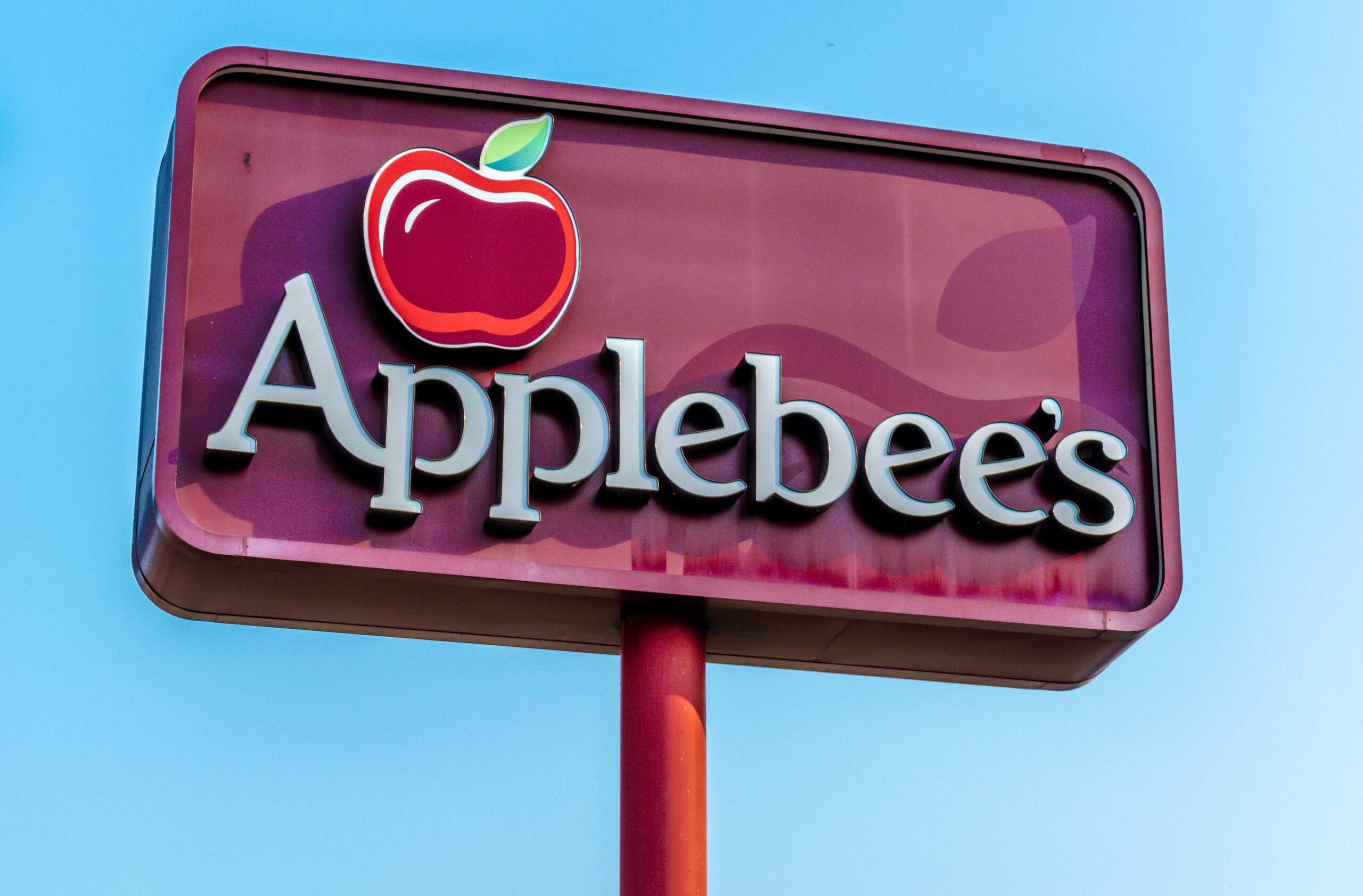Applebee’s restaurant sign with apple logo against blue sky.