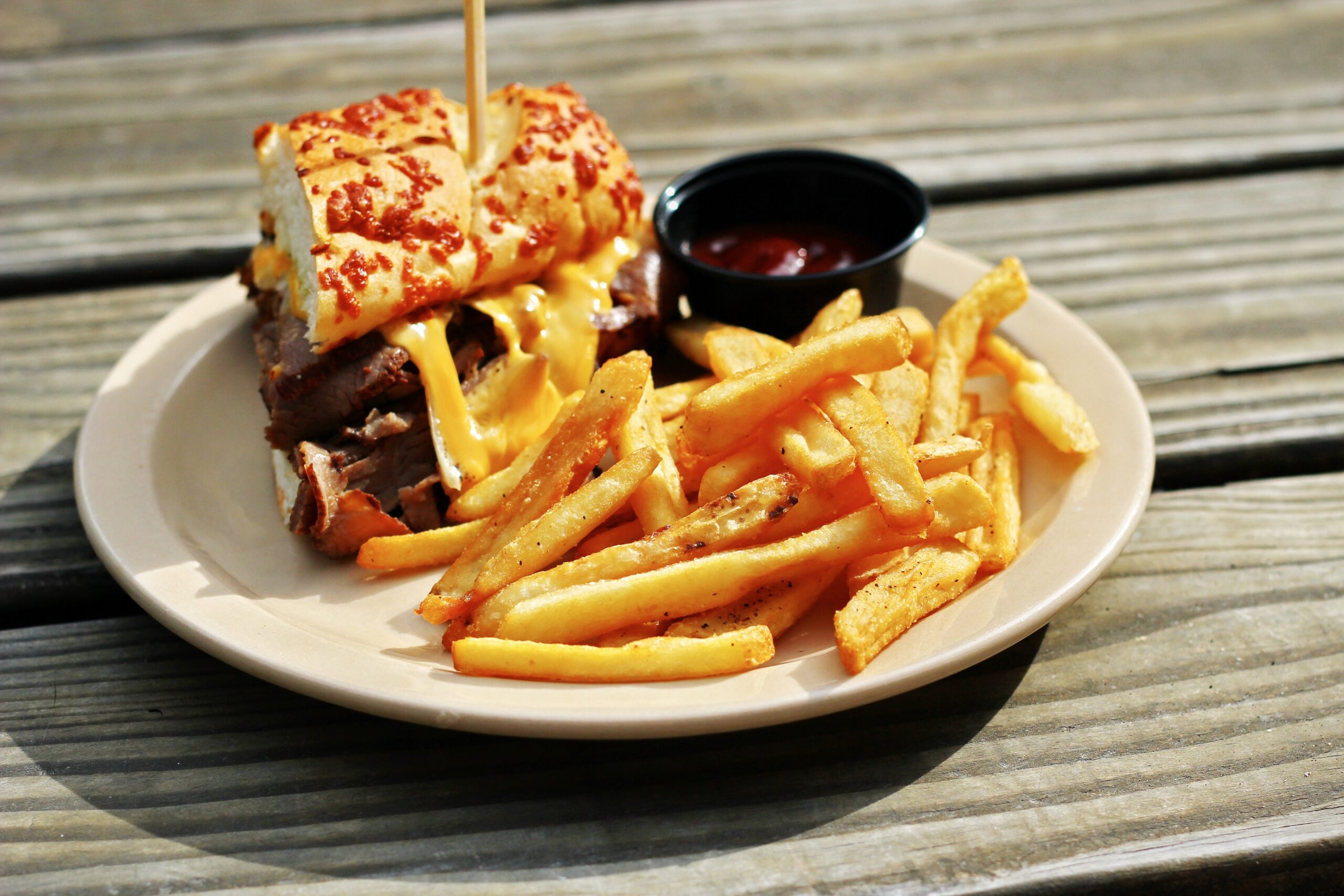 Cheesesteak sandwich with fries and ketchup on plate.