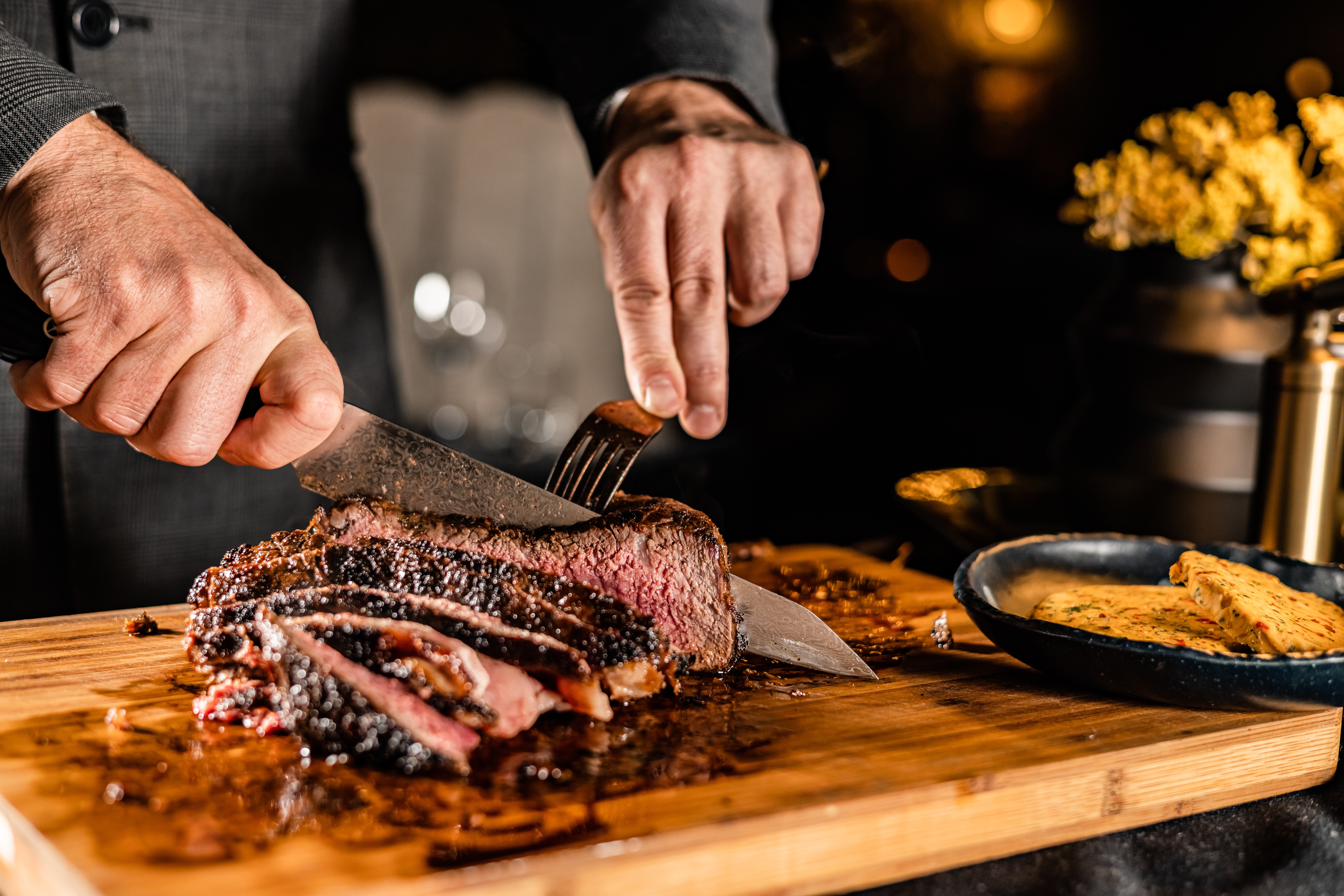 Chef slicing grilled steak on wooden board.