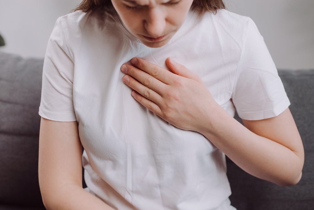 Une femme se tient la poitrine et se sent mal à l'aise lorsqu'elle est assise sur le canapé.