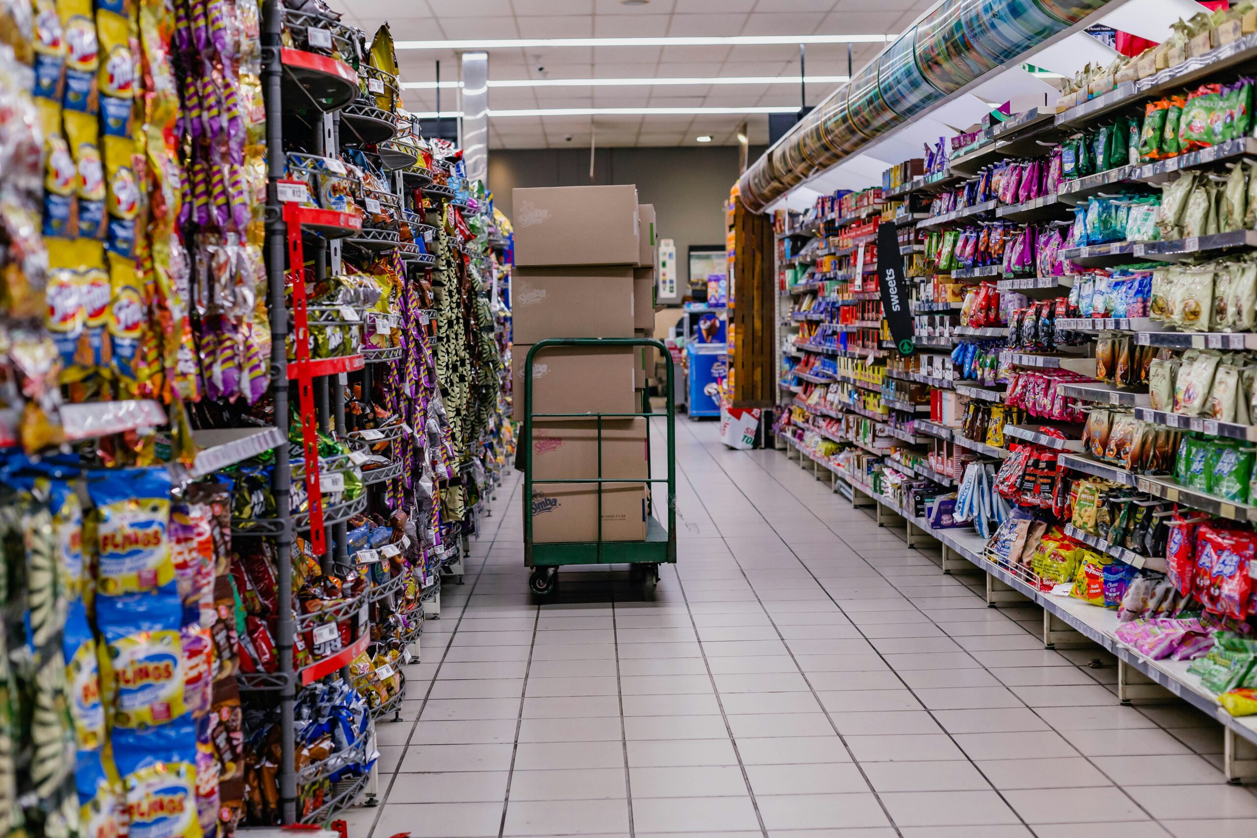 Grocery store aisle with snacks and cart of boxes.