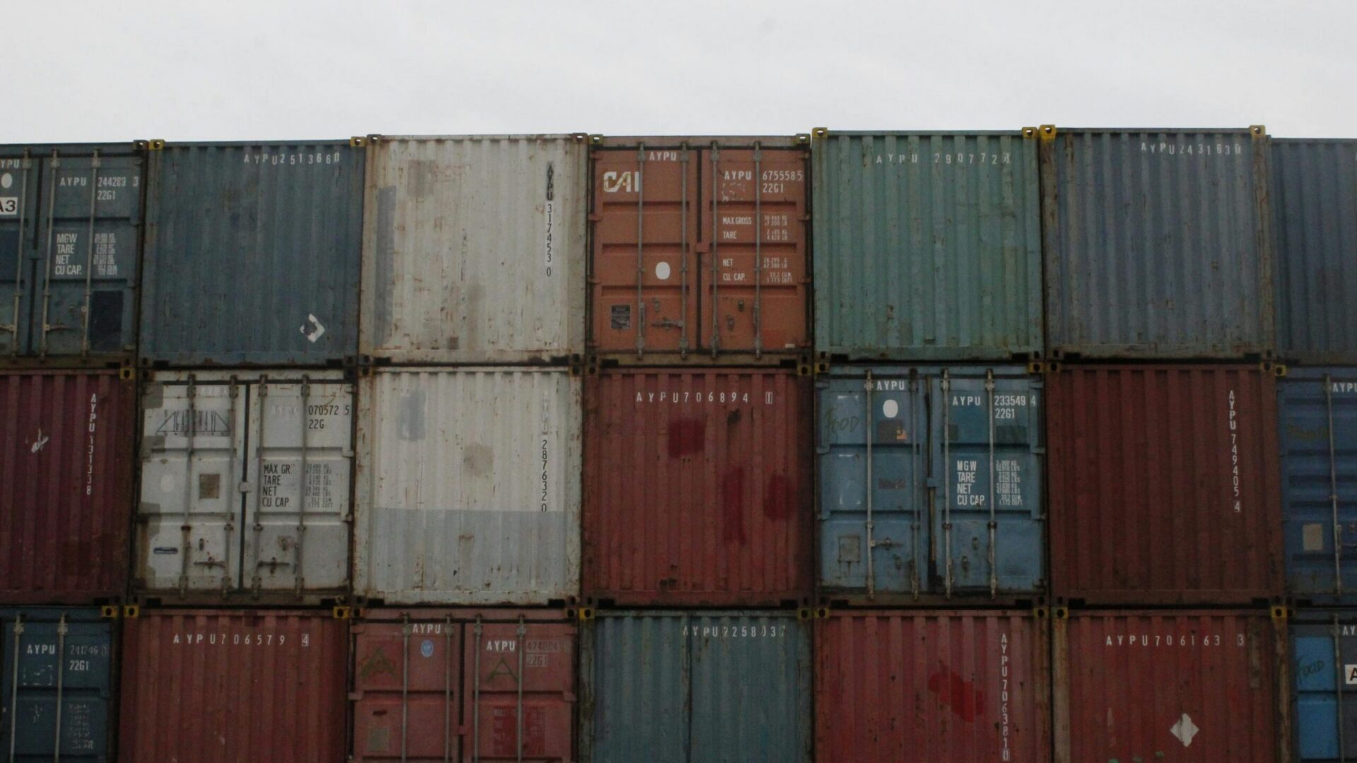 Stacked multicolored shipping containers forming a wall at an industrial storage site.