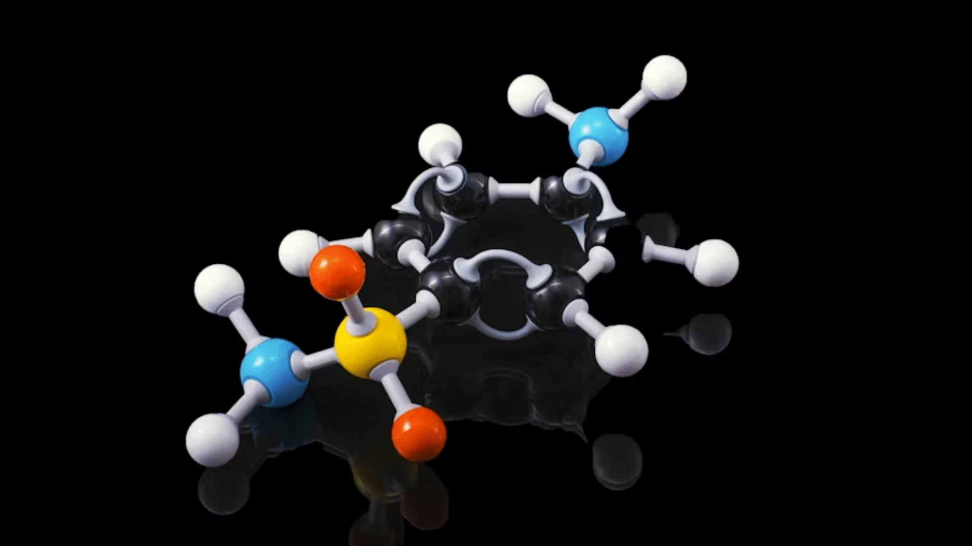 A professional high-definition photograph of a ball-and-stick molecular model against a reflective black background.