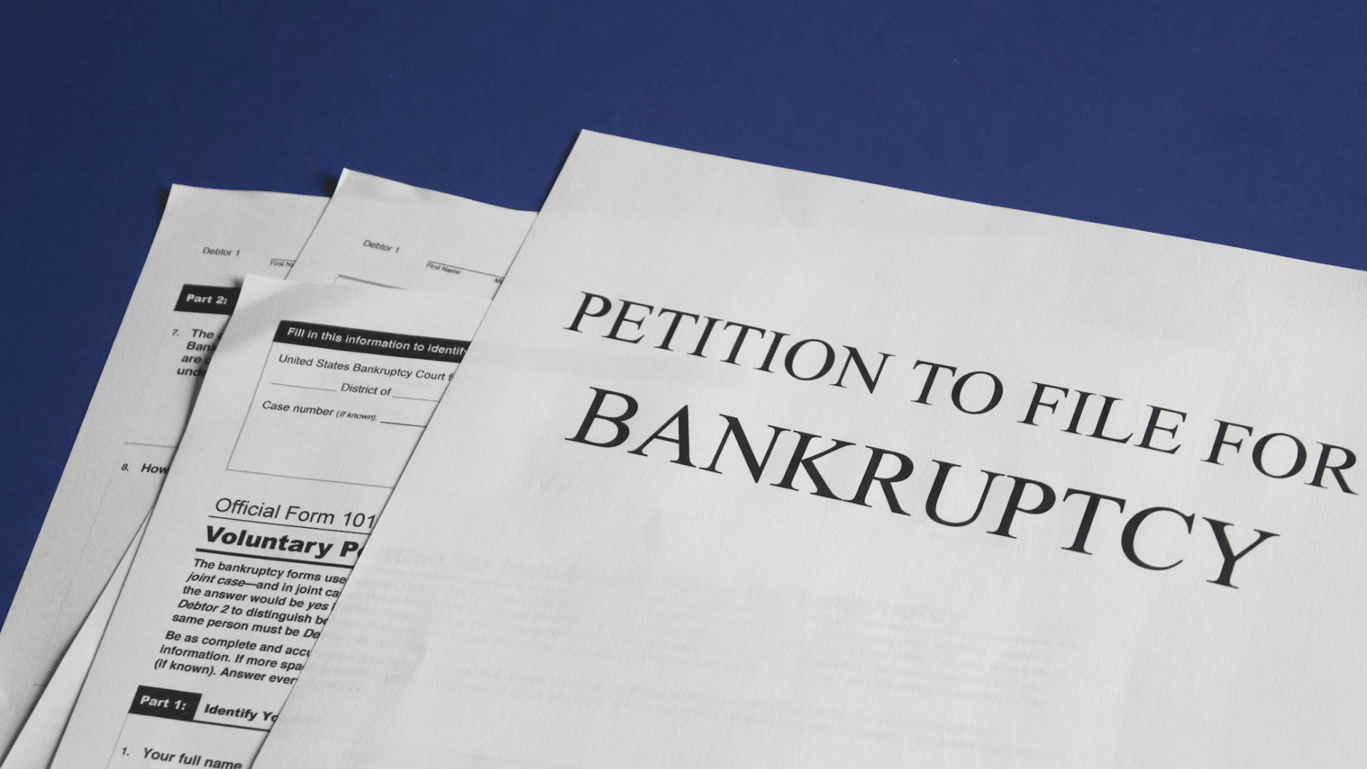 A close-up of legal documents, with the top page clearly titled "PETITION TO FILE FOR BANKRUPTCY."