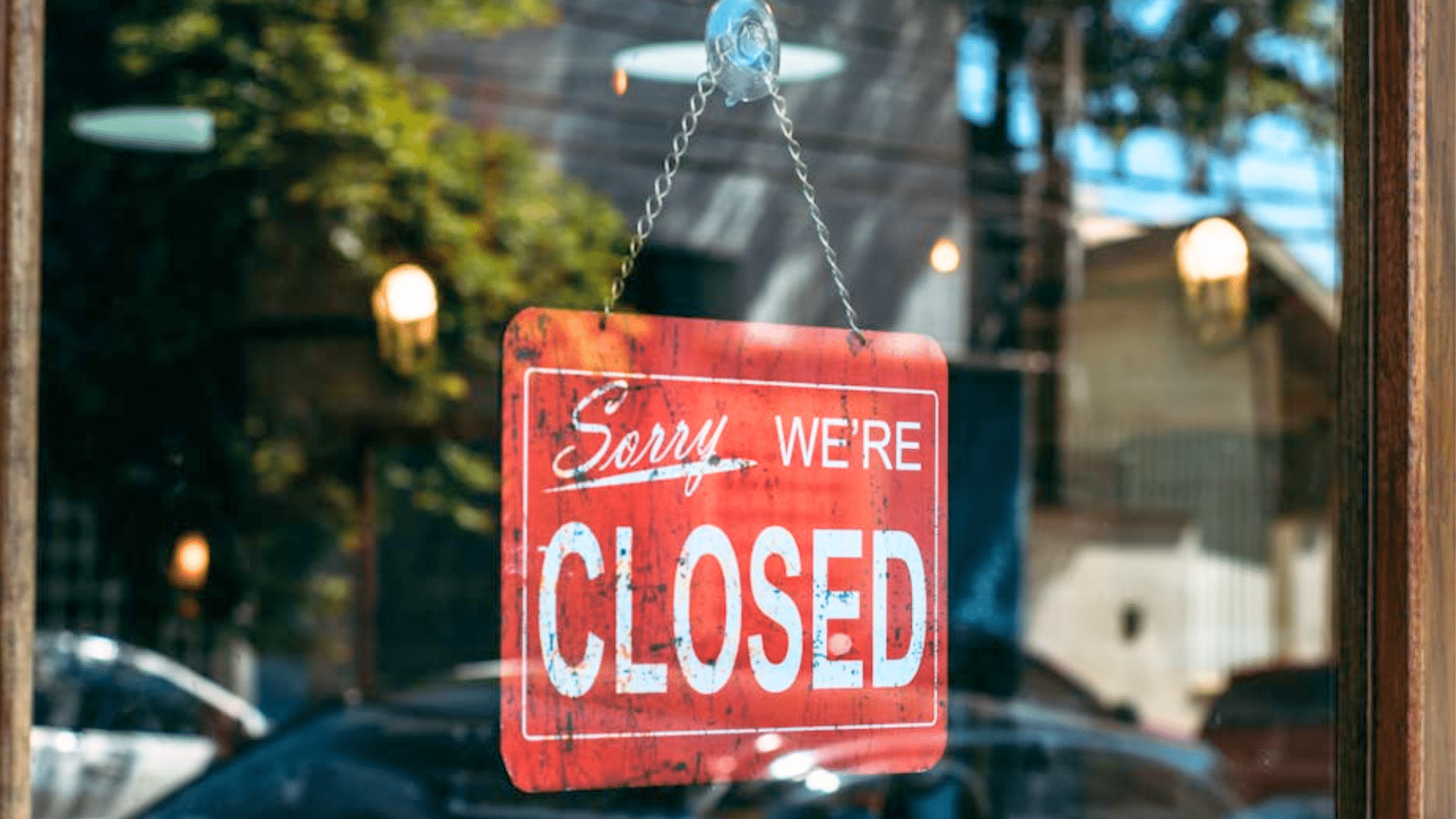 red "Sorry We're CLOSED" sign hanging inside a glass storefront window.