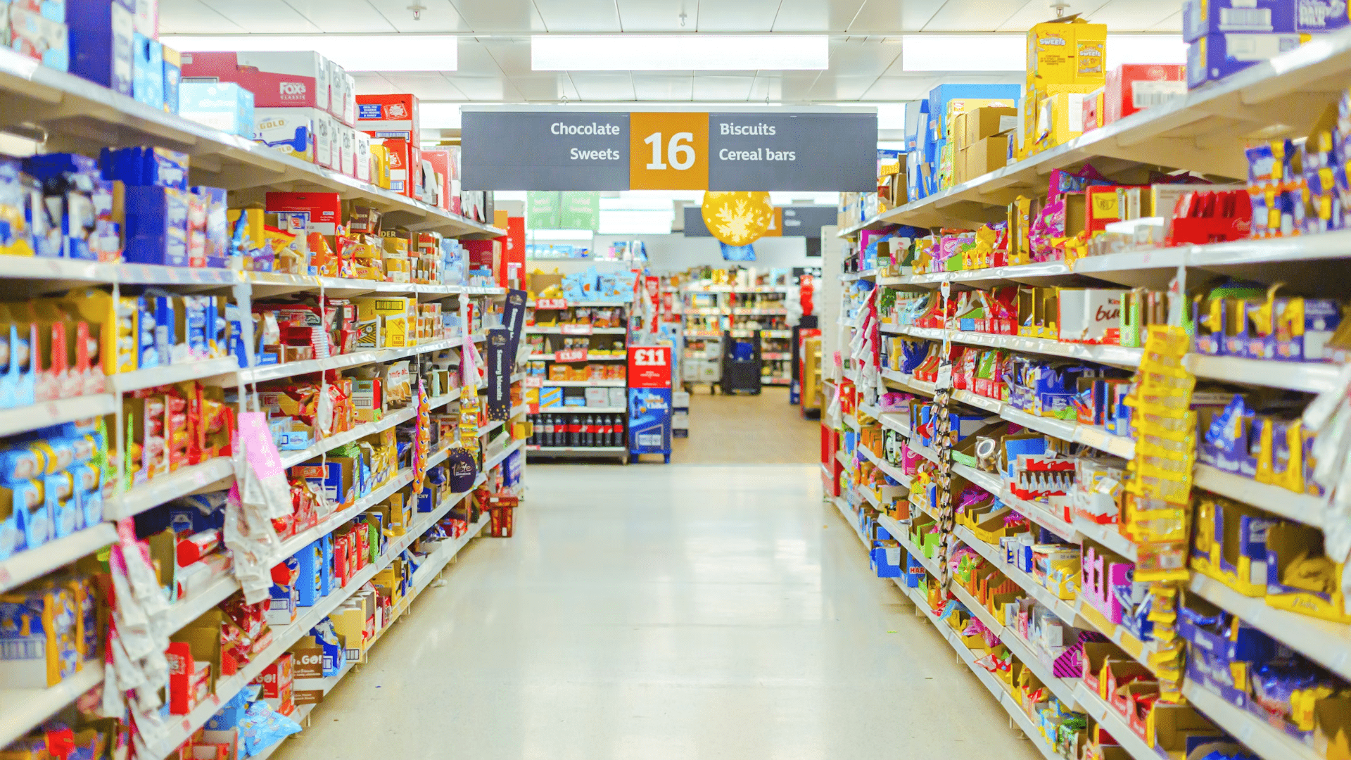 A long grocery store aisle packed with colorful packages of chocolates, sweets, and biscuits on the shelves.