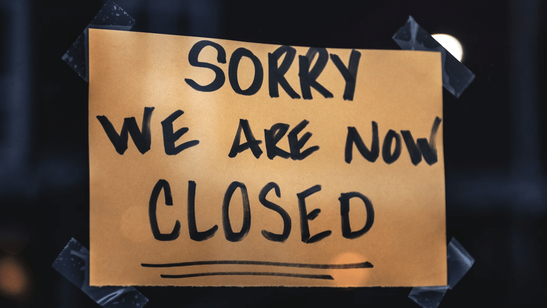 A handwritten brown paper sign taped to a dark window that reads "SORRY WE ARE NOW CLOSED."