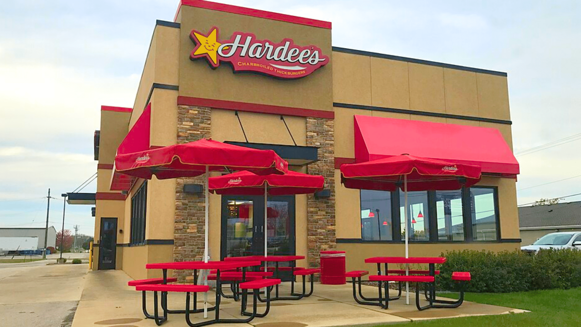 The exterior of a Hardee's restaurant featuring an outdoor patio with red umbrellas and red picnic tables.