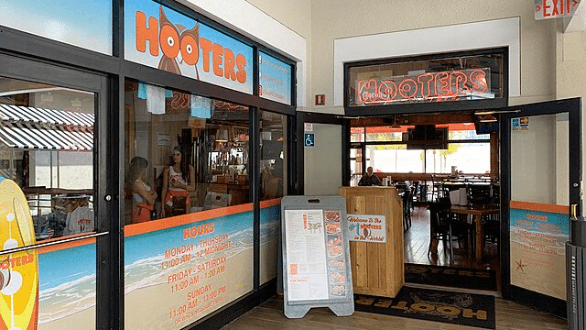 The entrance to a Hooters restaurant with open glass doors and a menu board outside.