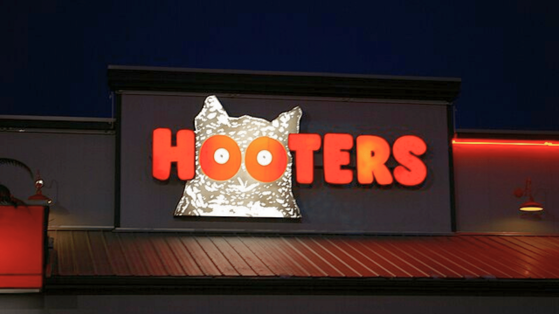 A glowing orange Hooters sign with a white owl logo on a building at night.