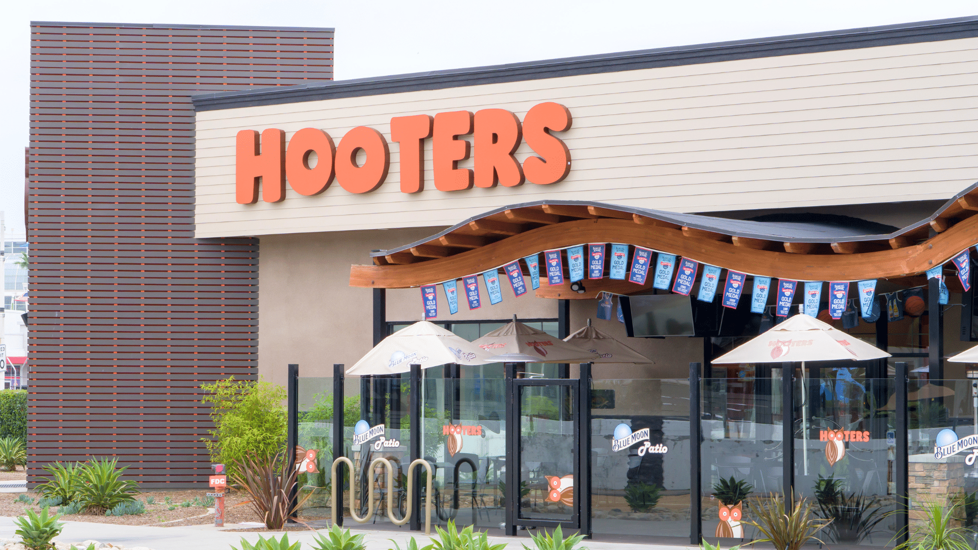 The outside of a Hooters restaurant featuring an outdoor patio dining area with umbrellas.