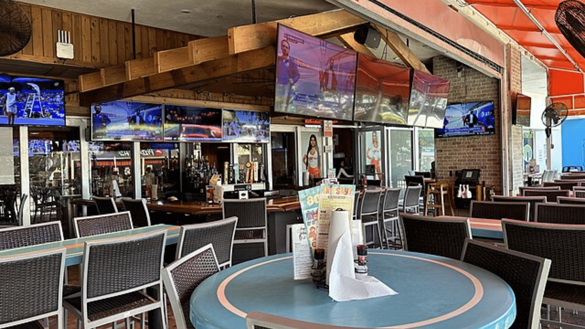 An empty covered patio at a Hooters restaurant with tables, chairs, a bar, and multiple TVs.