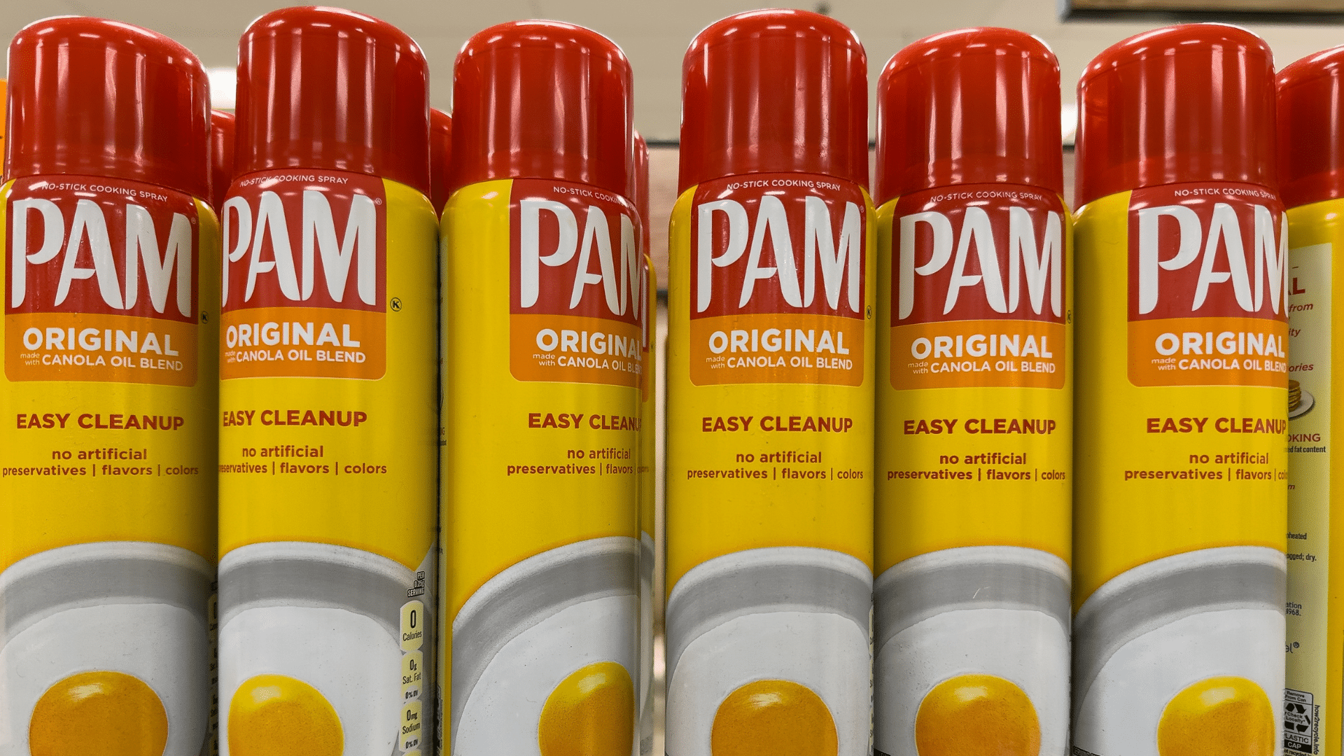 A row of yellow PAM cooking spray cans sits on a shelf.