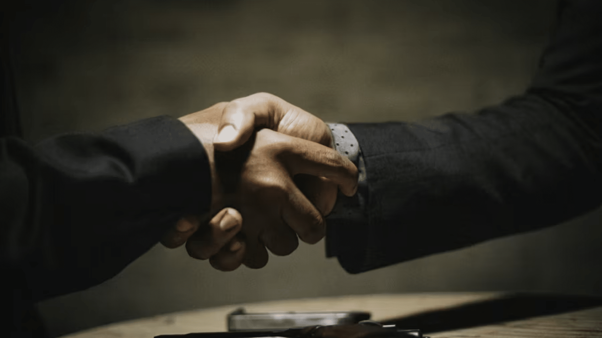 A dramatic close-up of a firm handshake between two people in dark business suits, symbolizing a significant corporate agreement or the closing of a major partnership.