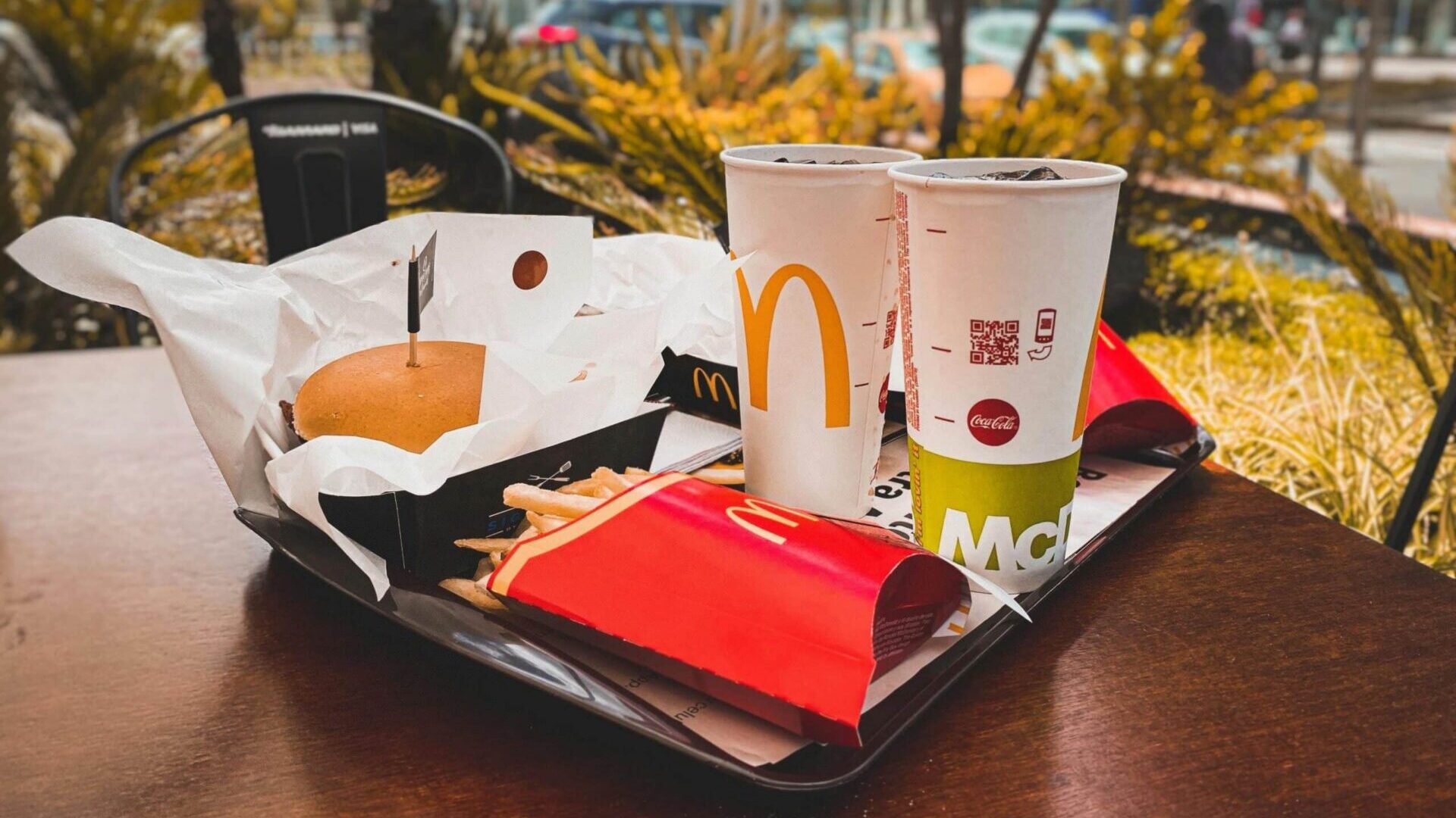 McDonald’s meal with burger box, fries, and two drinks on a tray at an outdoor table.