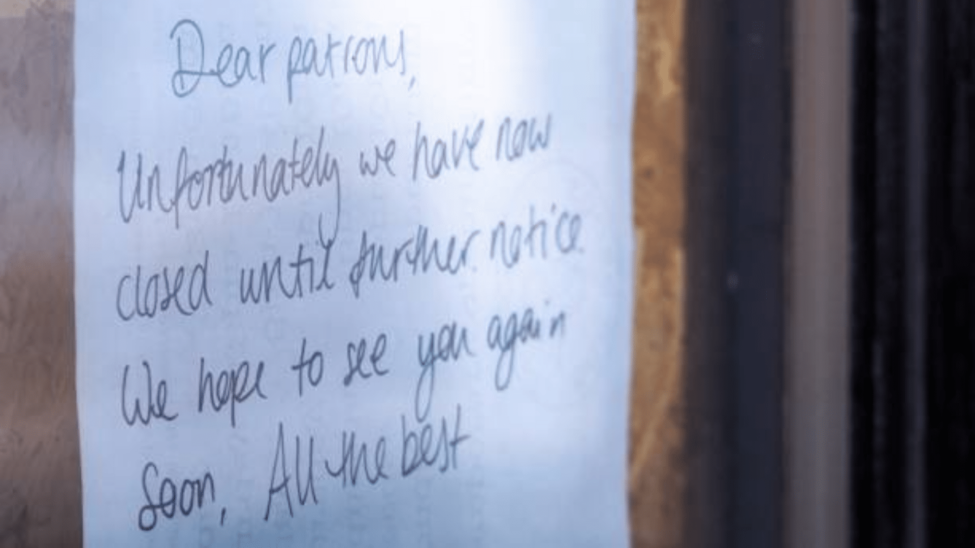 A handwritten note taped to a glass door.