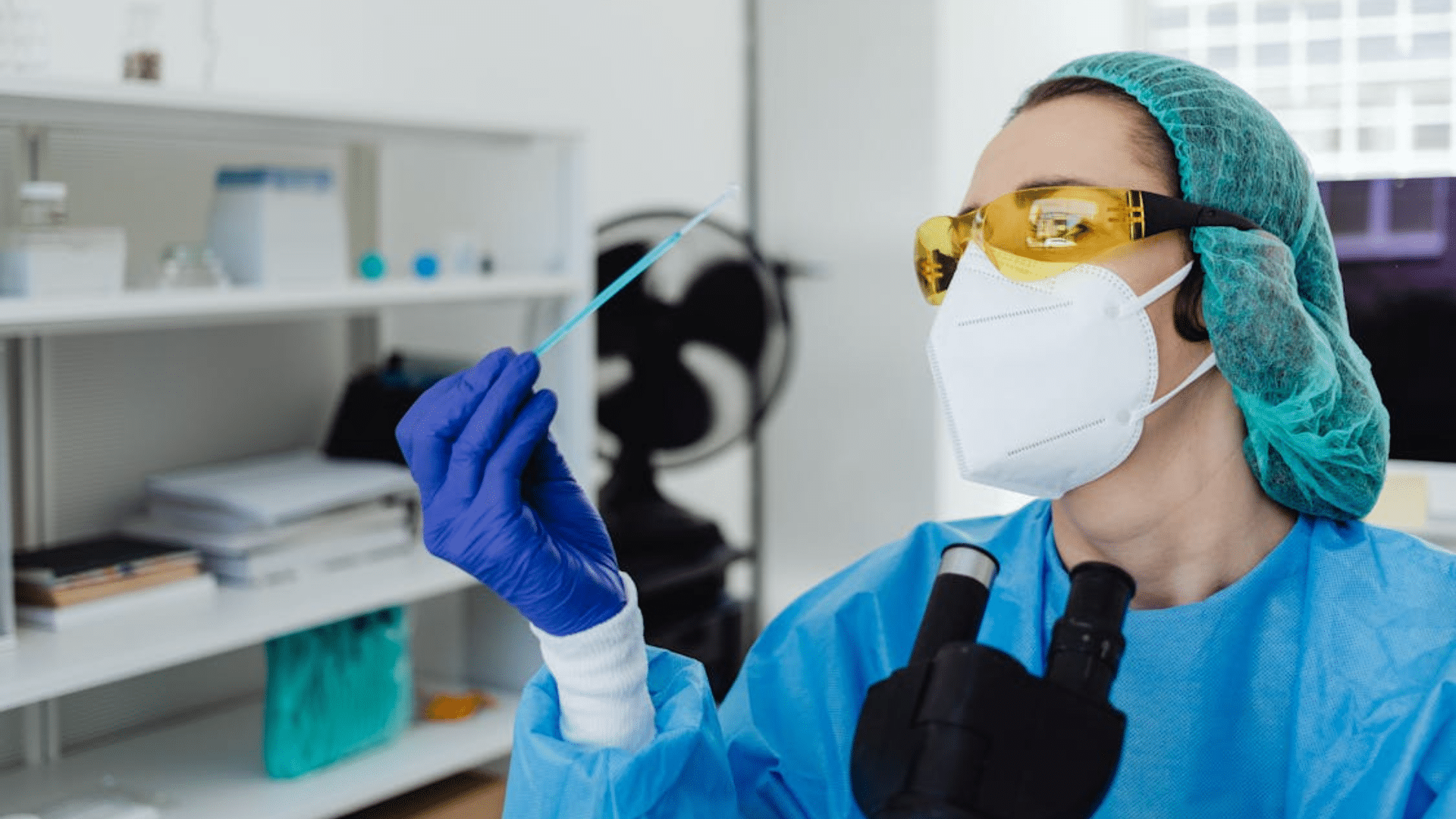 A person wearing safety gear looks closely at a small blue swab.