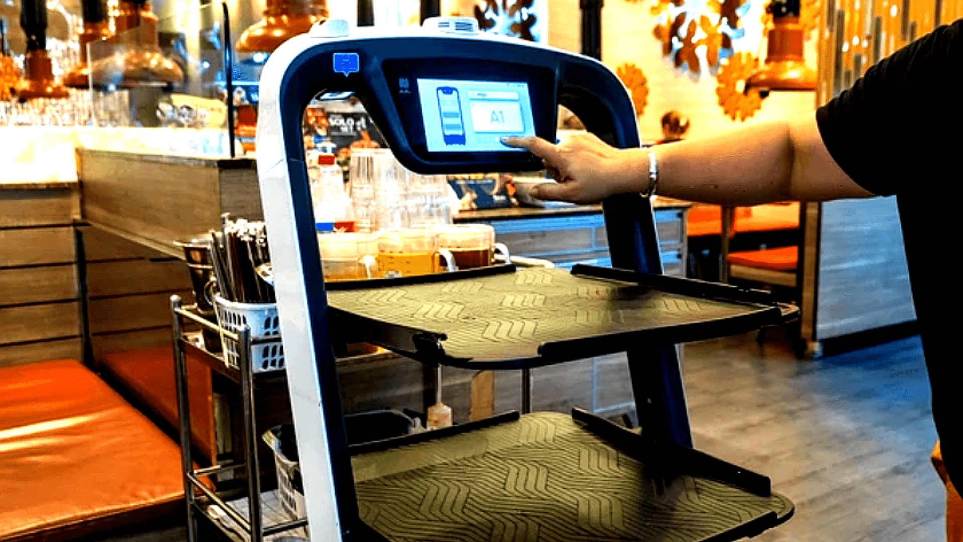 Person interacting with touchscreen on service robot cart inside restaurant.