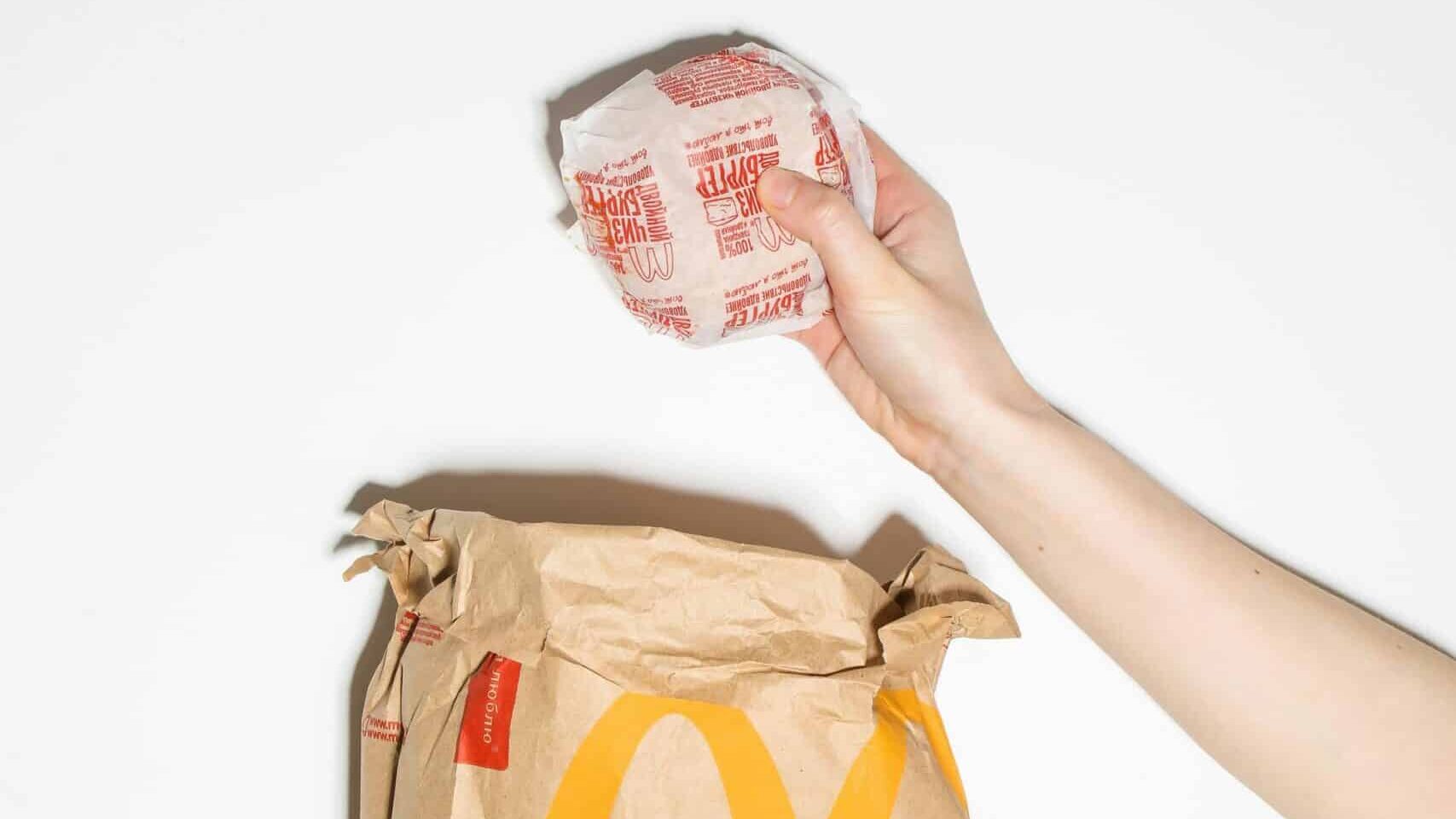 Hand holding a McDonald’s drink cup above a paper takeout bag with McDonald’s logo.