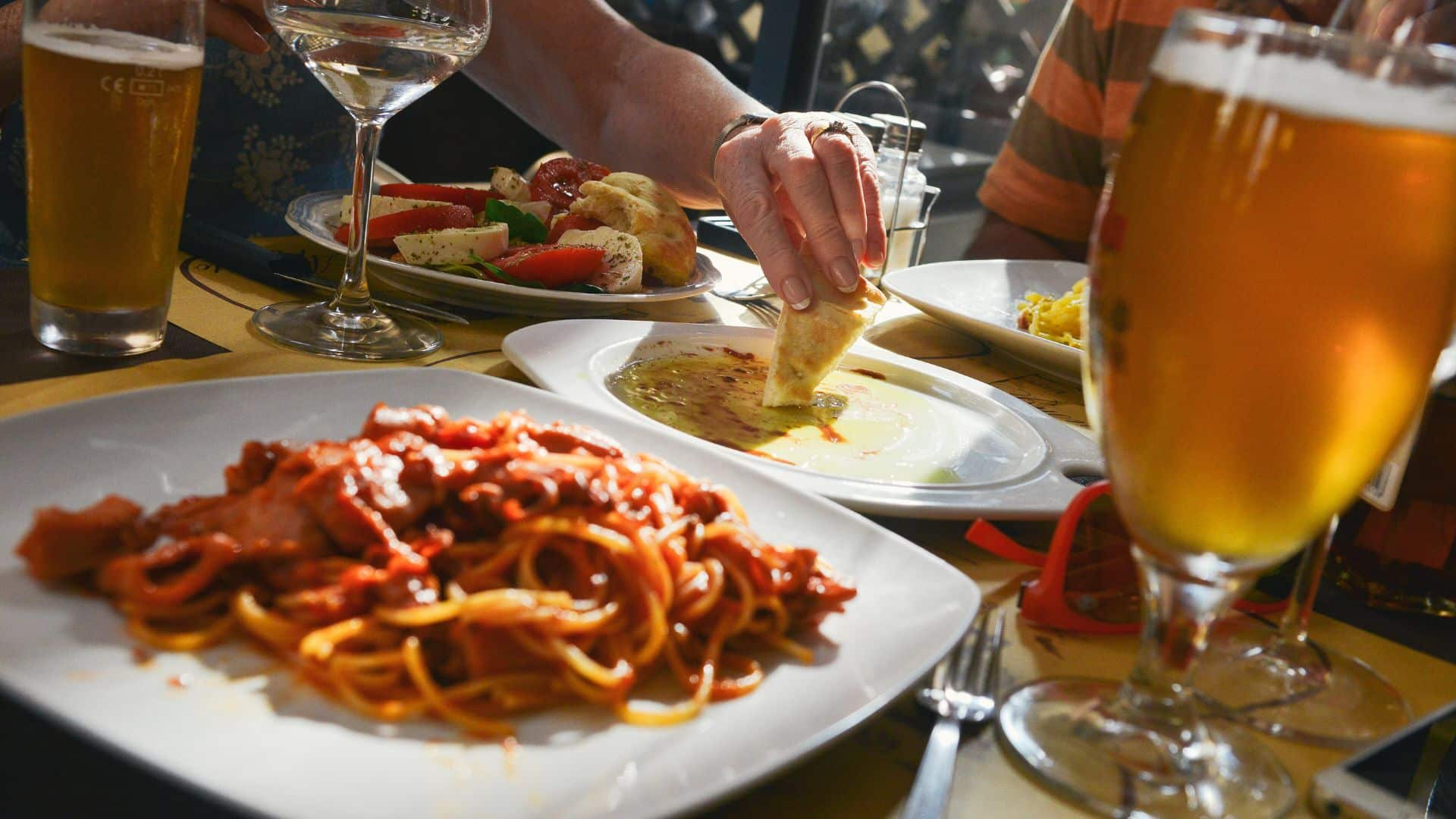 Plate of spaghetti with tomato sauce on a restaurant table alongside beer and wine glasses.