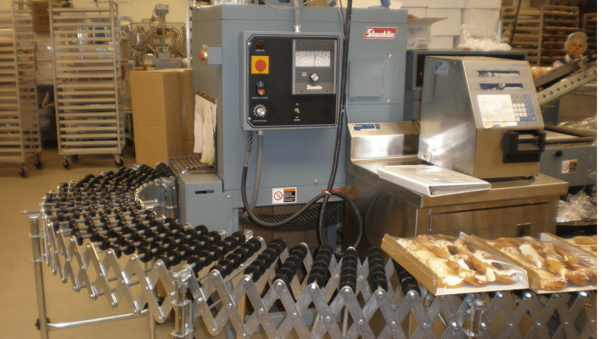 An industrial conveyor belt system in a commercial bakery processes trays of freshly packaged pastries.