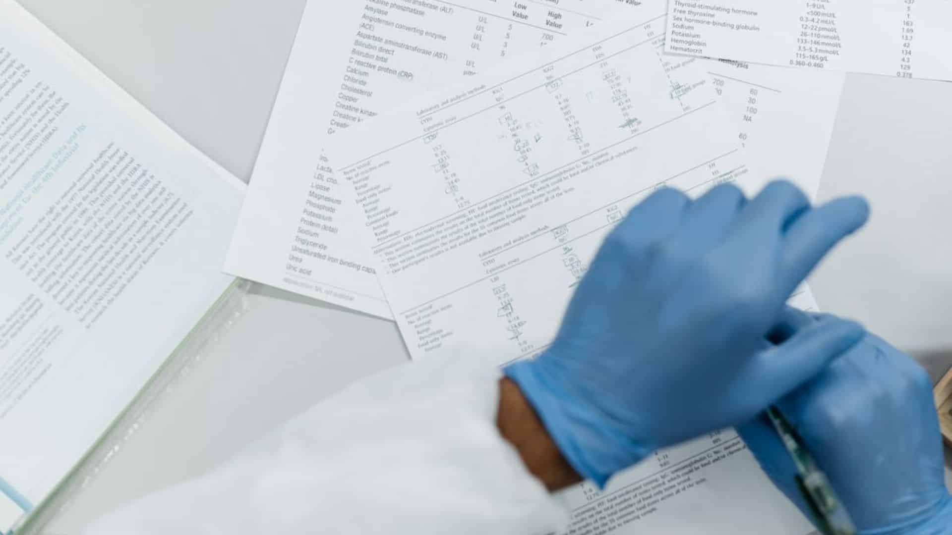 Gloved hands reviewing clinical data and lab result sheets on a white surface.
