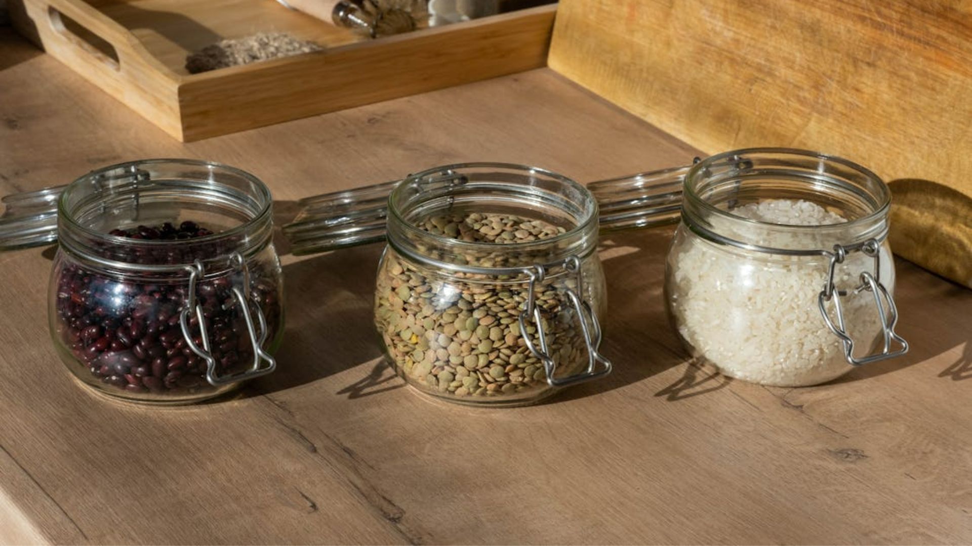 Clear glass jars with raw beans, seeds, and rice on a brown wooden table.