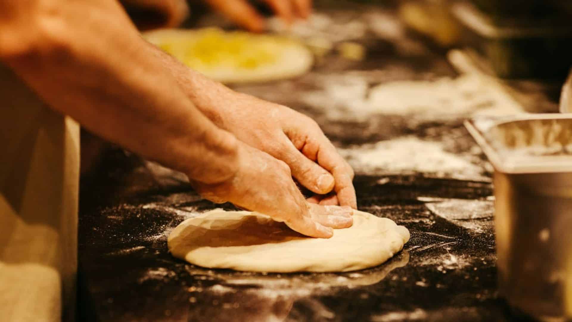 A close up of a person's hands stretching pizza dough on a counter with flour.
