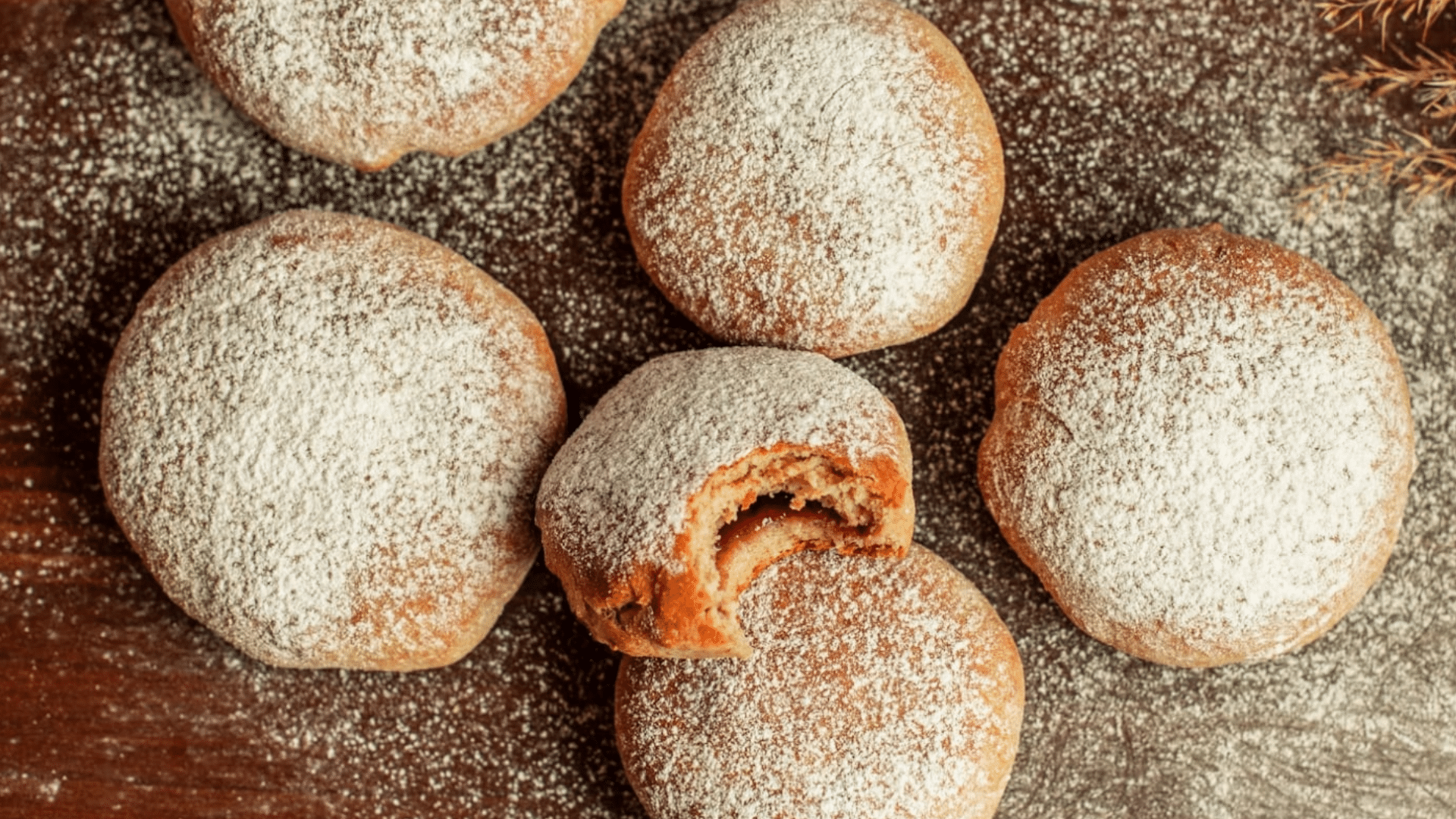 Top-down view of raspberry-filled sugar cookies dusted with powdered sugar on a wooden table.