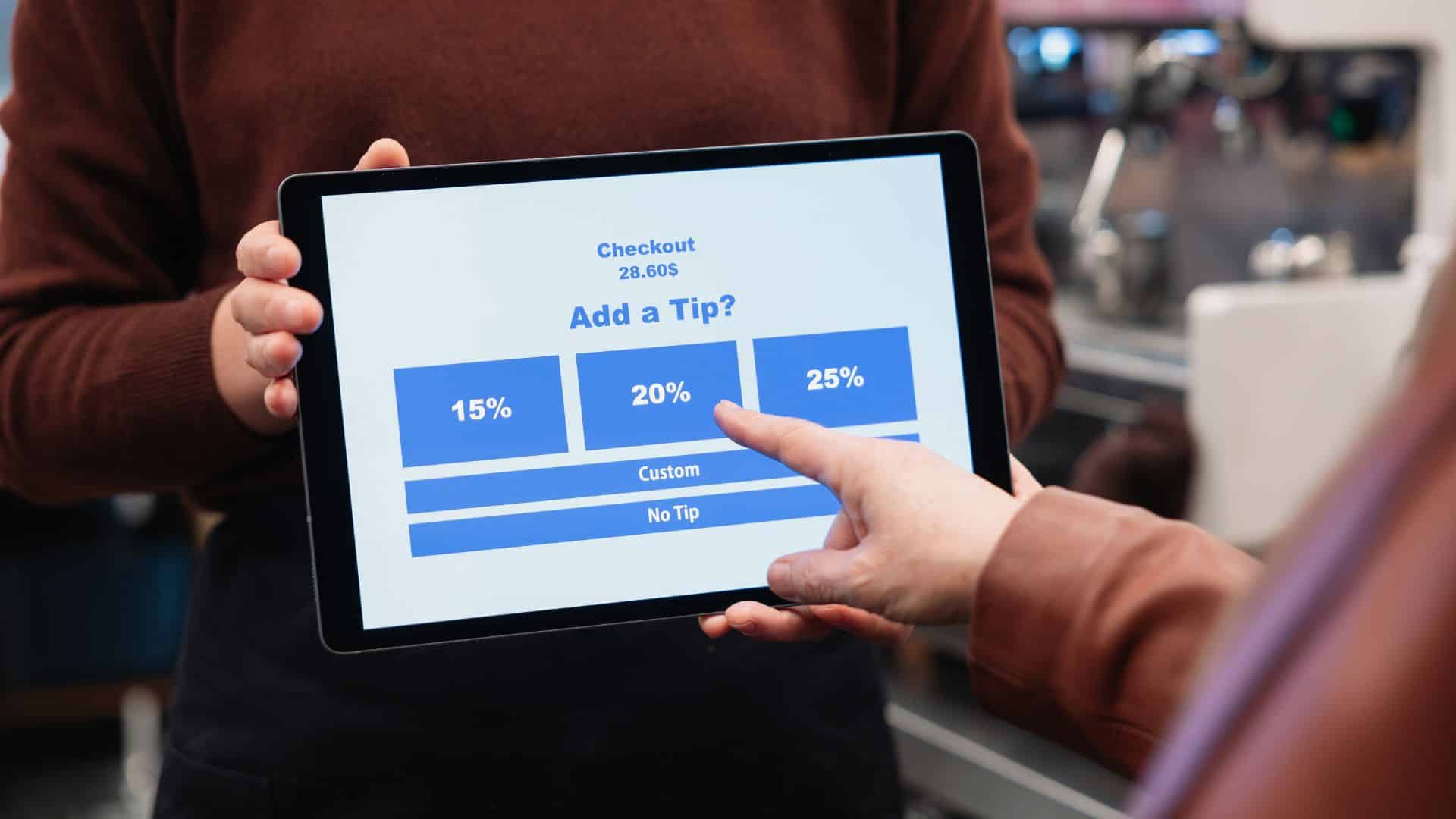 Employee holding tablet for tip payment in cafe and customer touching it to pay tip.