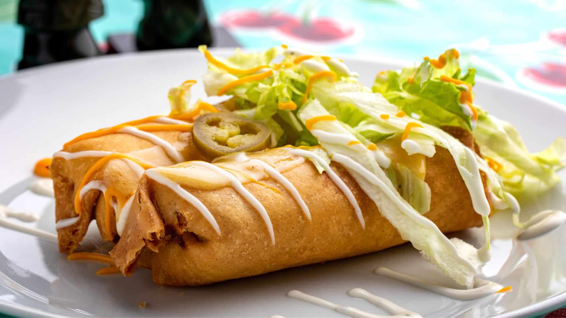 Golden fried burritos topped with cream sauce shredded cheese and fresh lettuce.