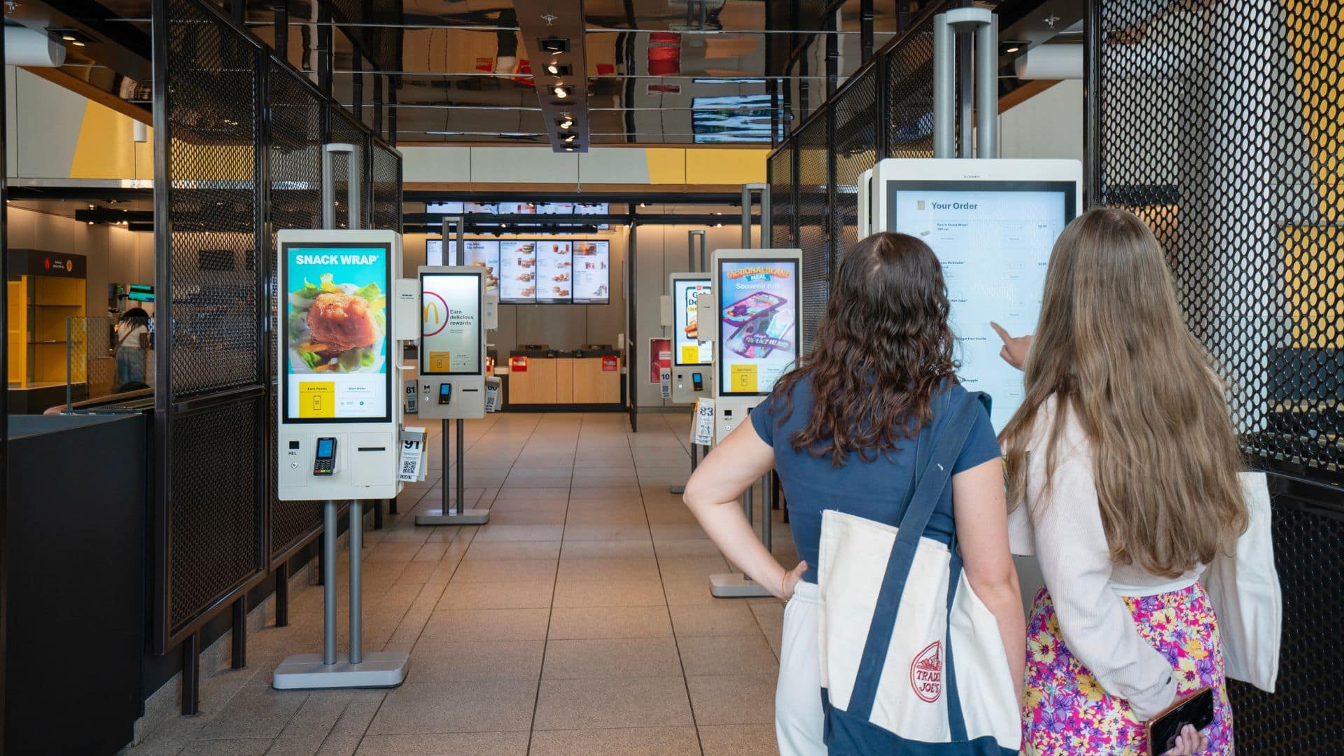 Two customers browsing self-service kiosks inside a McDonald's restaurant.