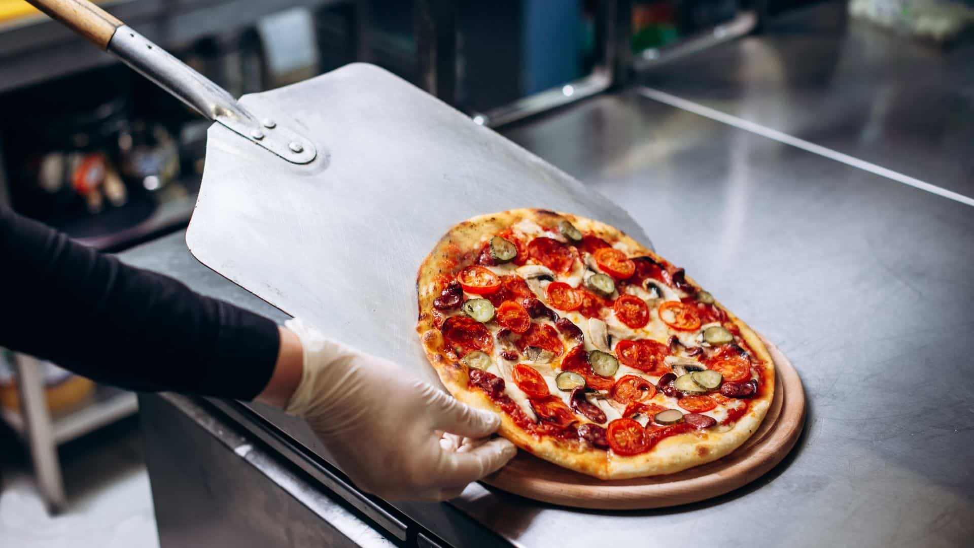 A fresh-out-of-the-oven pizza topped with an assortment of toppings is placed on a wooden board.